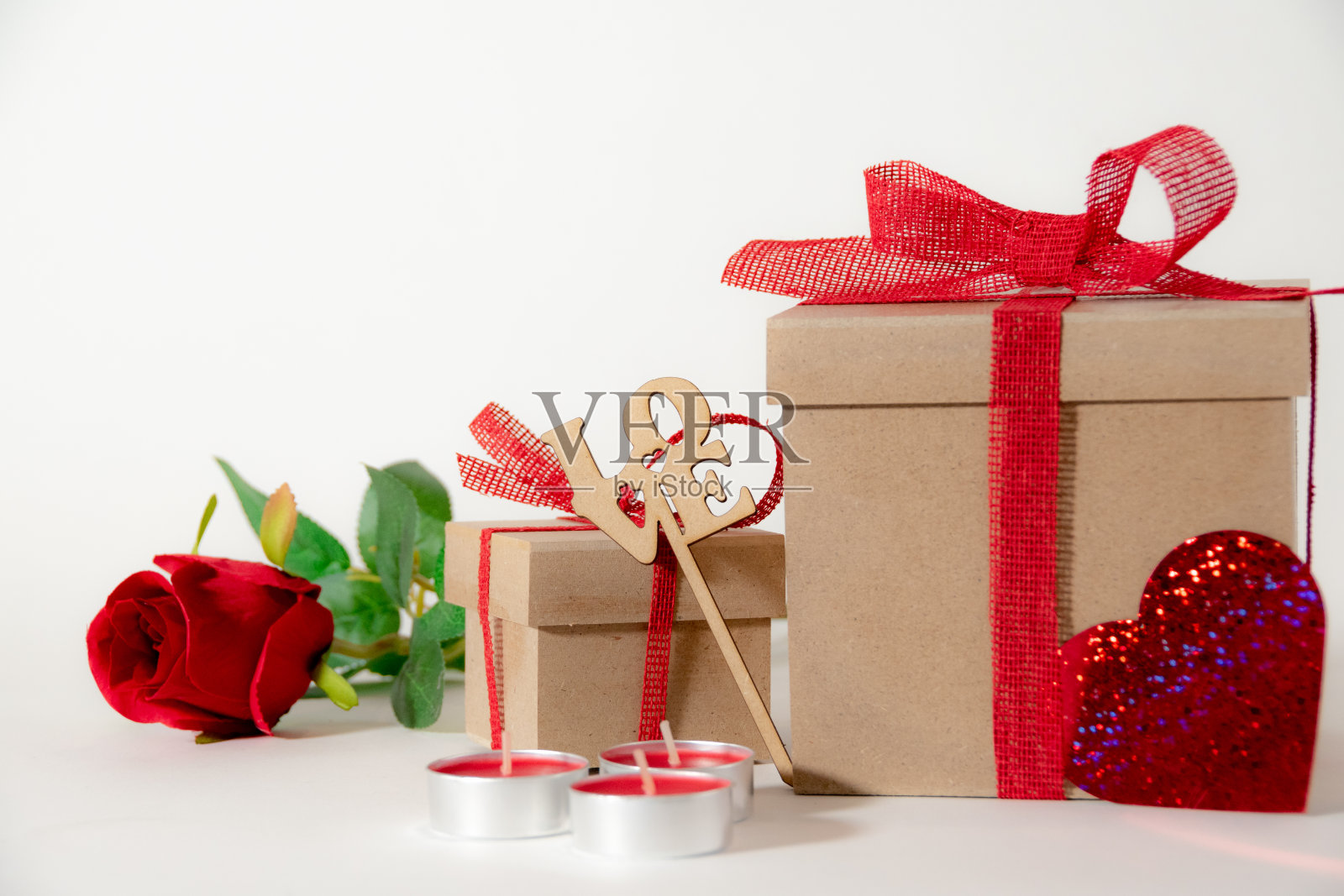 白色背景上的礼物盒、红丝带、装饰心、玫瑰和红色蜡烛特写照片摄影图片