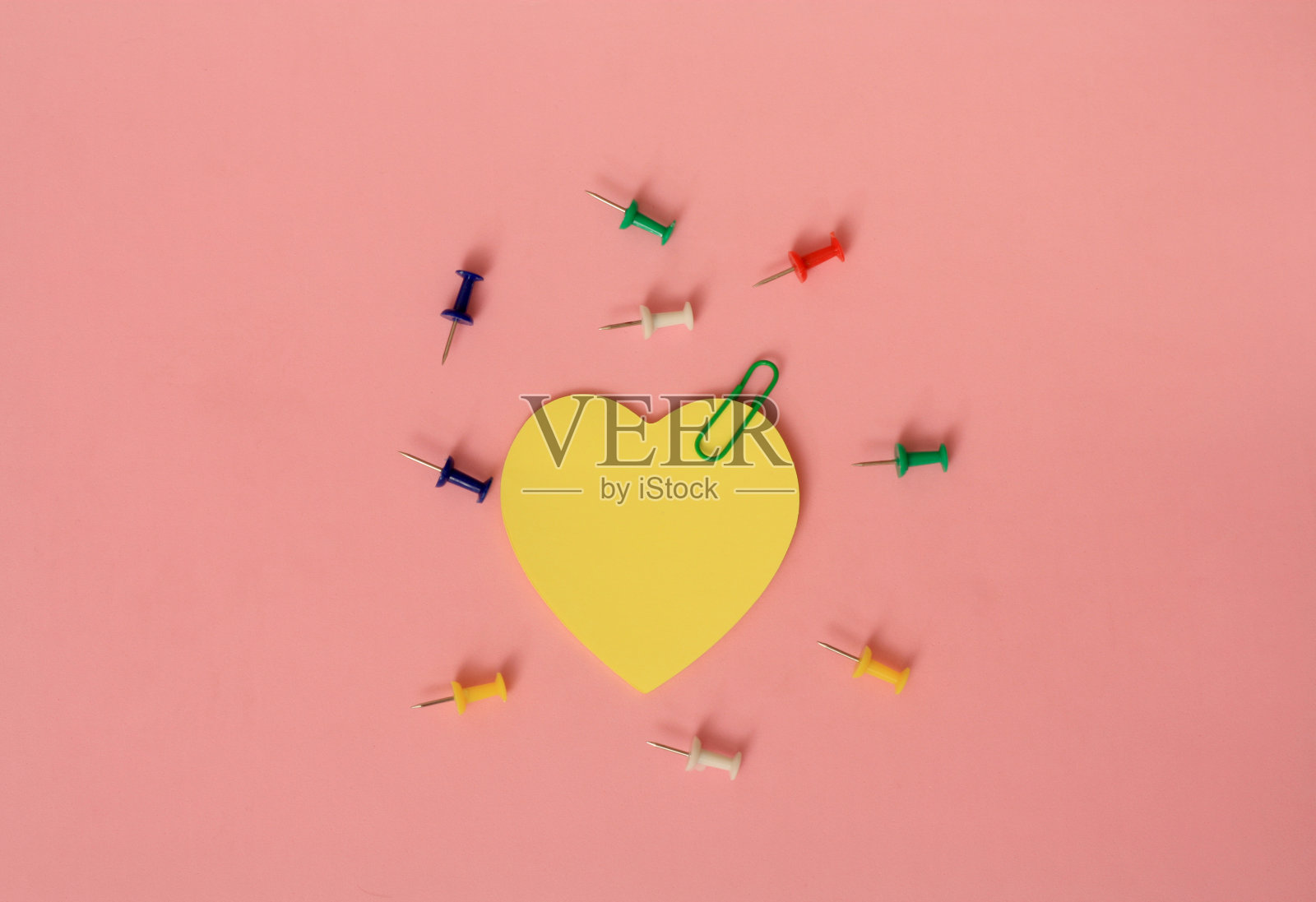 顶部视图空白黄色笔记纸与回形针和多颜色图钉在粉红色的桌子上。照片摄影图片