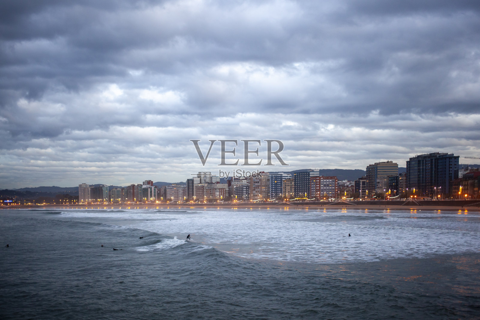 落日在圣洛伦佐德Gijón的海滩上，冲浪者掀起了海浪照片摄影图片