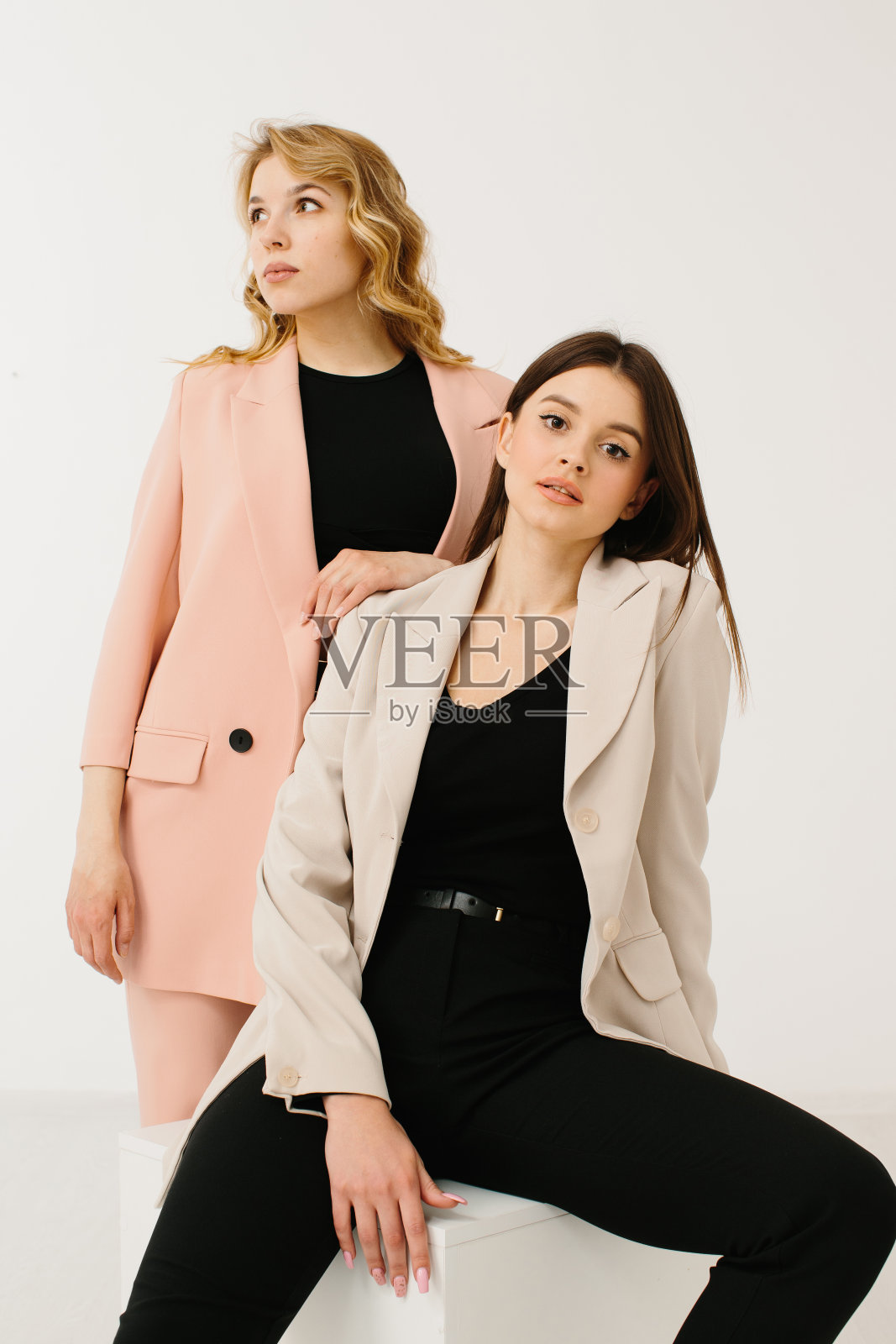 模特们穿着时尚的柔和的运动夹克和裤子，穿着时尚的运动鞋，在工作室的白色背景下的一个立方体上摆姿势。照片摄影图片