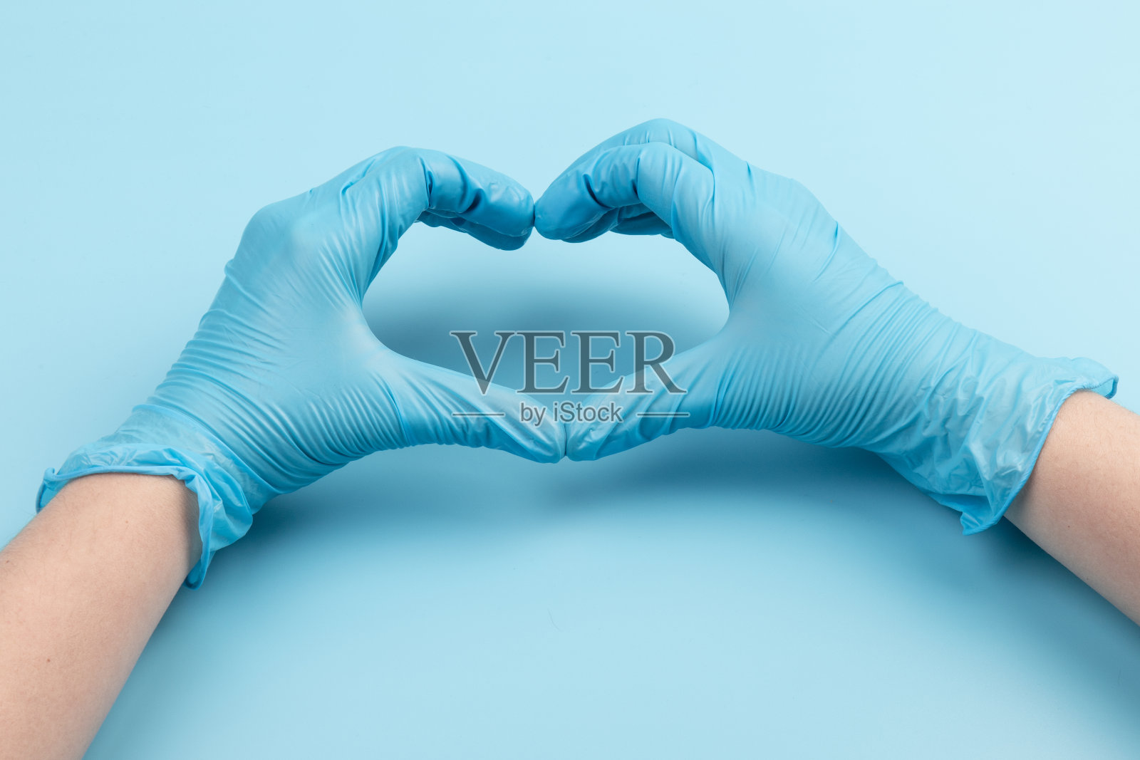 医生的手在医疗手套的形状在蓝色背景与复制空间的心脏。照片摄影图片