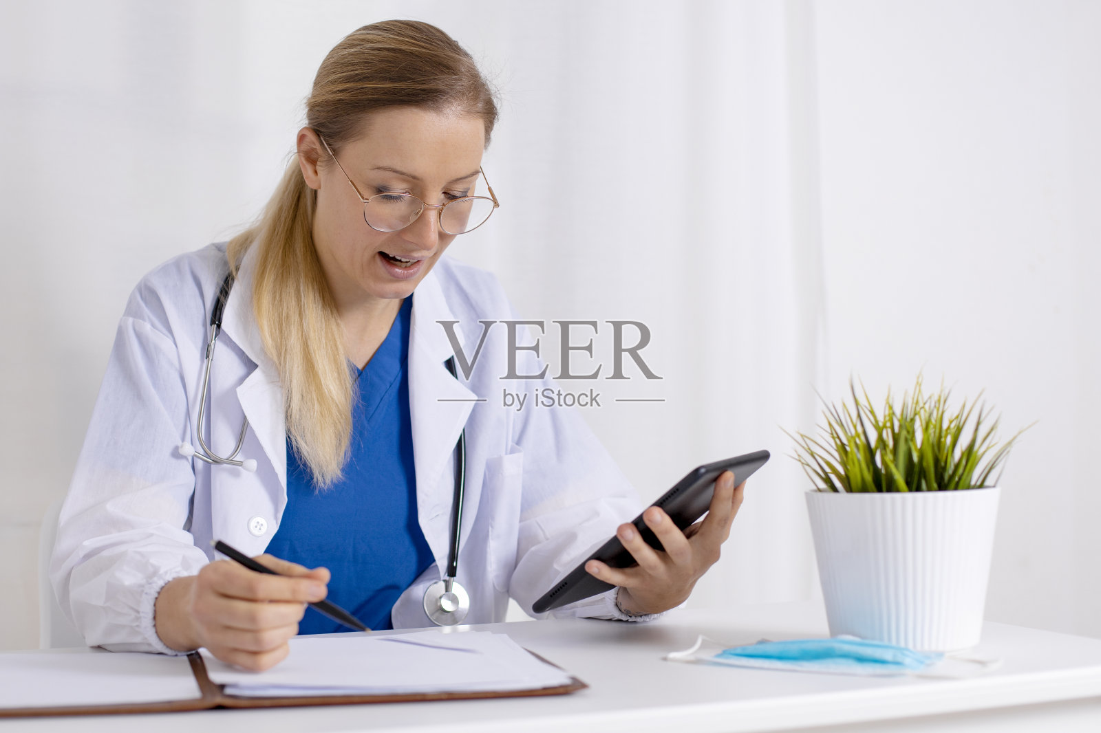 年轻女医生用平板电脑与病人在线交谈。咨询、视频通话、距离。Covid-19期间的医疗保健。白大褂医生，听诊器，随时待命。照片摄影图片