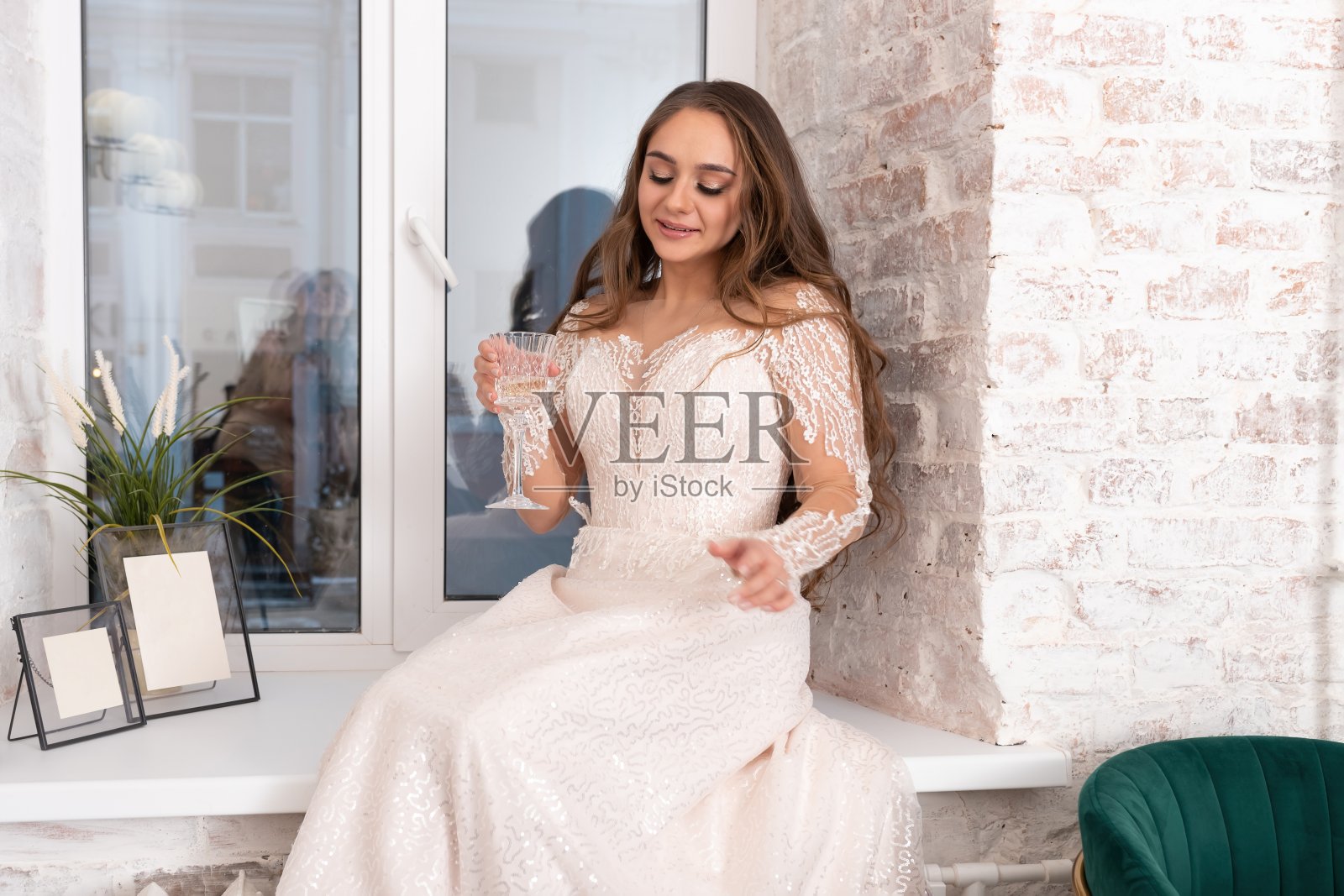 新娘端着一杯酒坐在窗台上。照片摄影图片