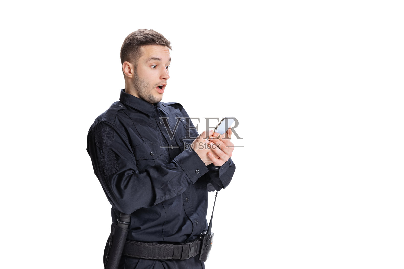 震惊的年轻人，穿着黑色制服的警察用白色背景的手机。工作观念、事业观念、法律秩序观念。照片摄影图片