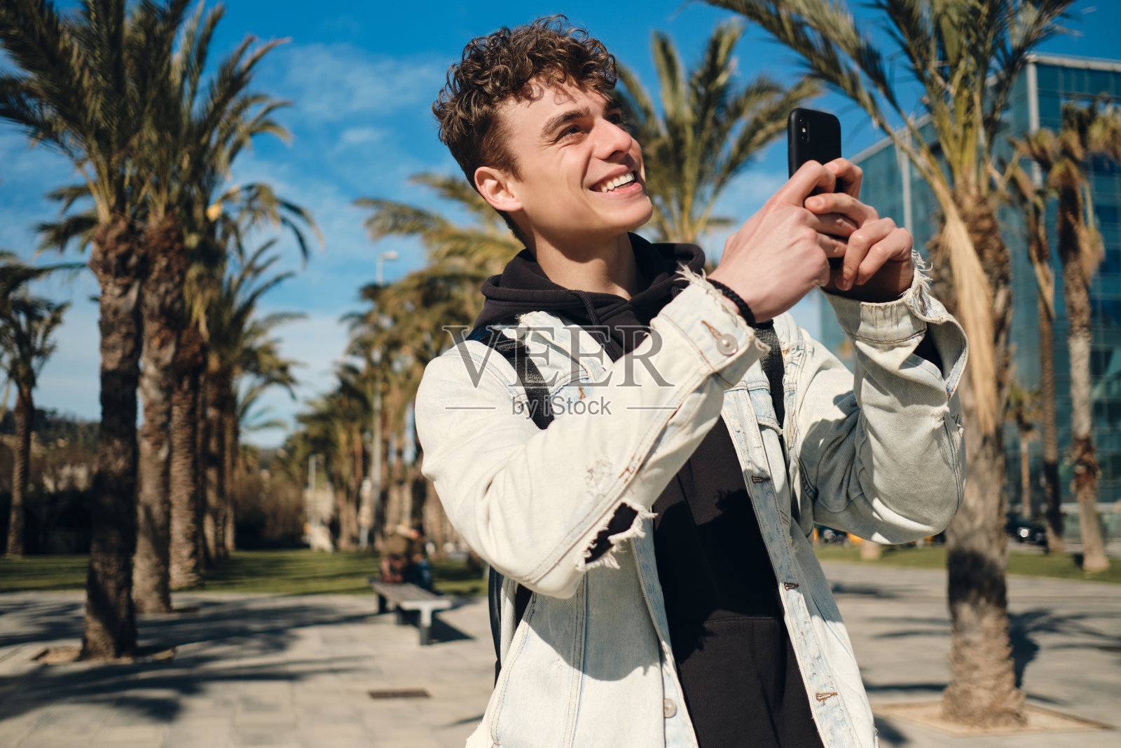 有魅力的家伙在有棕榈树的街道上开心地用智能手机拍照照片摄影图片