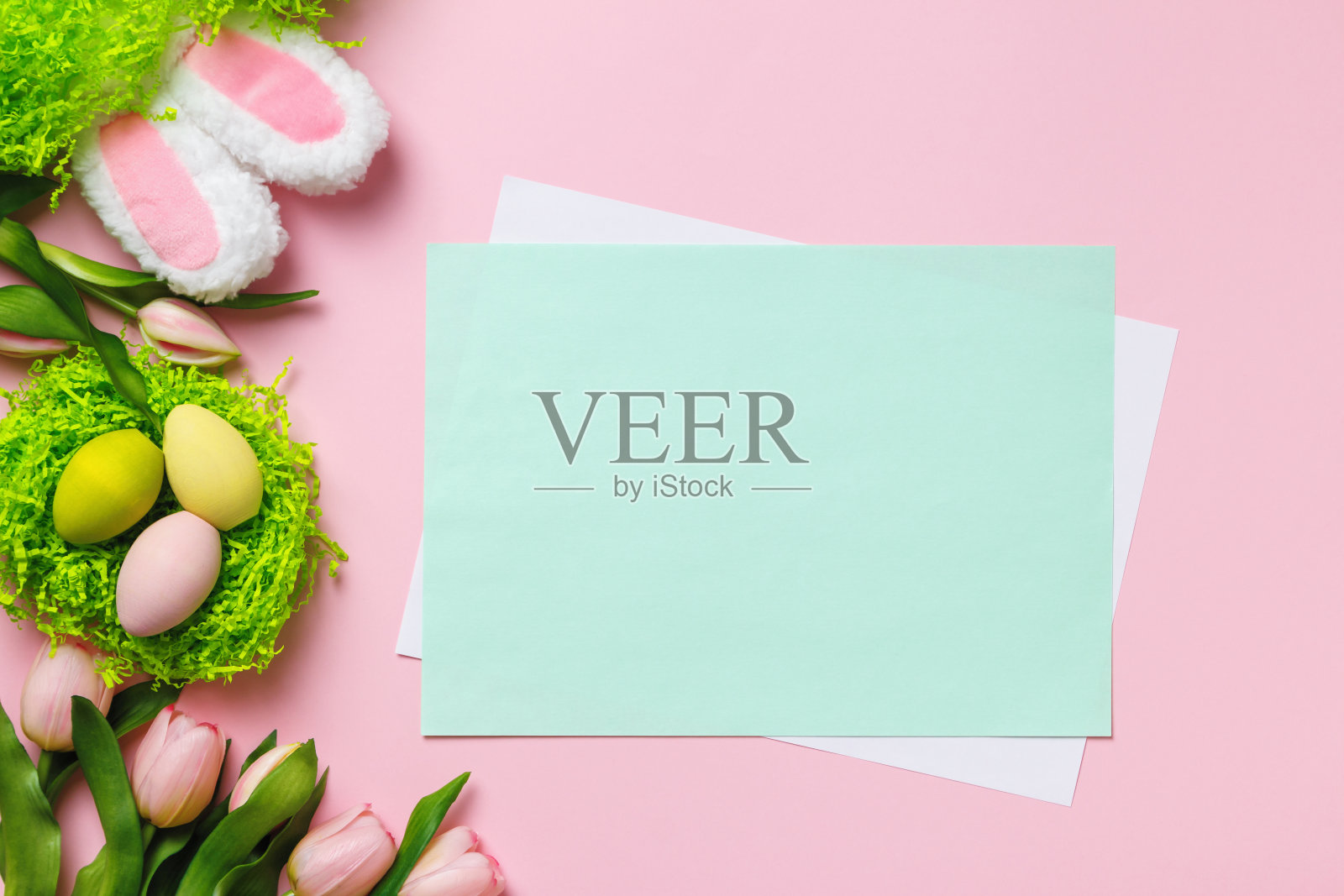 复活节组成。在粉红色的背景上，在郁金香花兔耳朵的鸟巢里的多色蛋。留出文字和拷贝空间的空白纸照片摄影图片