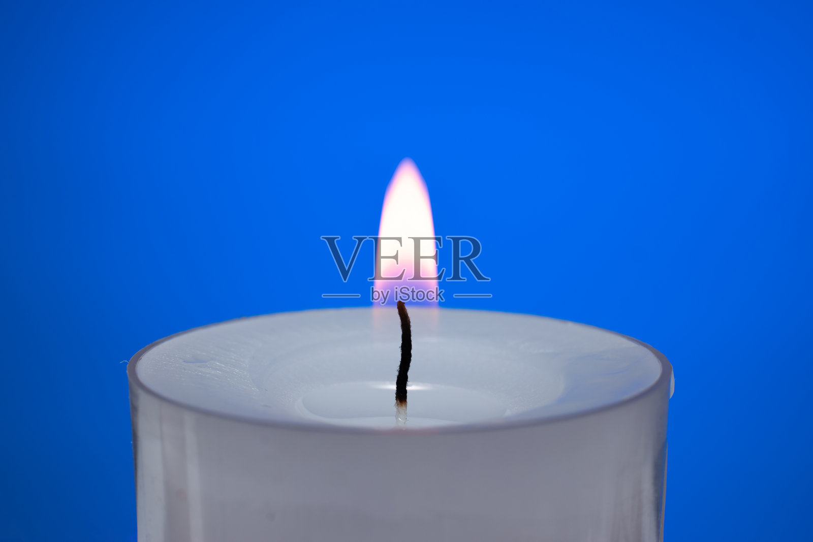 一支白色的小蜡烛在燃烧。近景摄影，孤立在蓝色背景上照片摄影图片