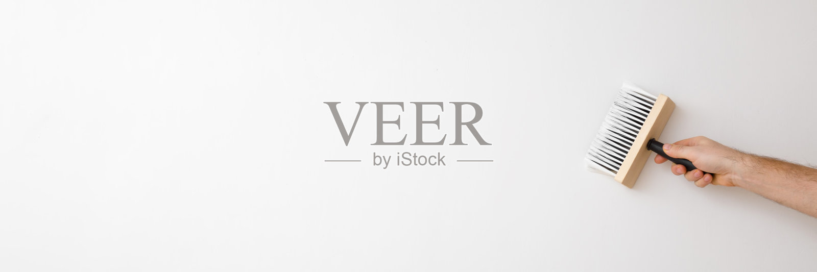 年轻的成年男子用刷子在白色的墙壁上涂胶水做壁纸。特写镜头。家庭维修工作。宽横幅。文本的空白位置。照片摄影图片