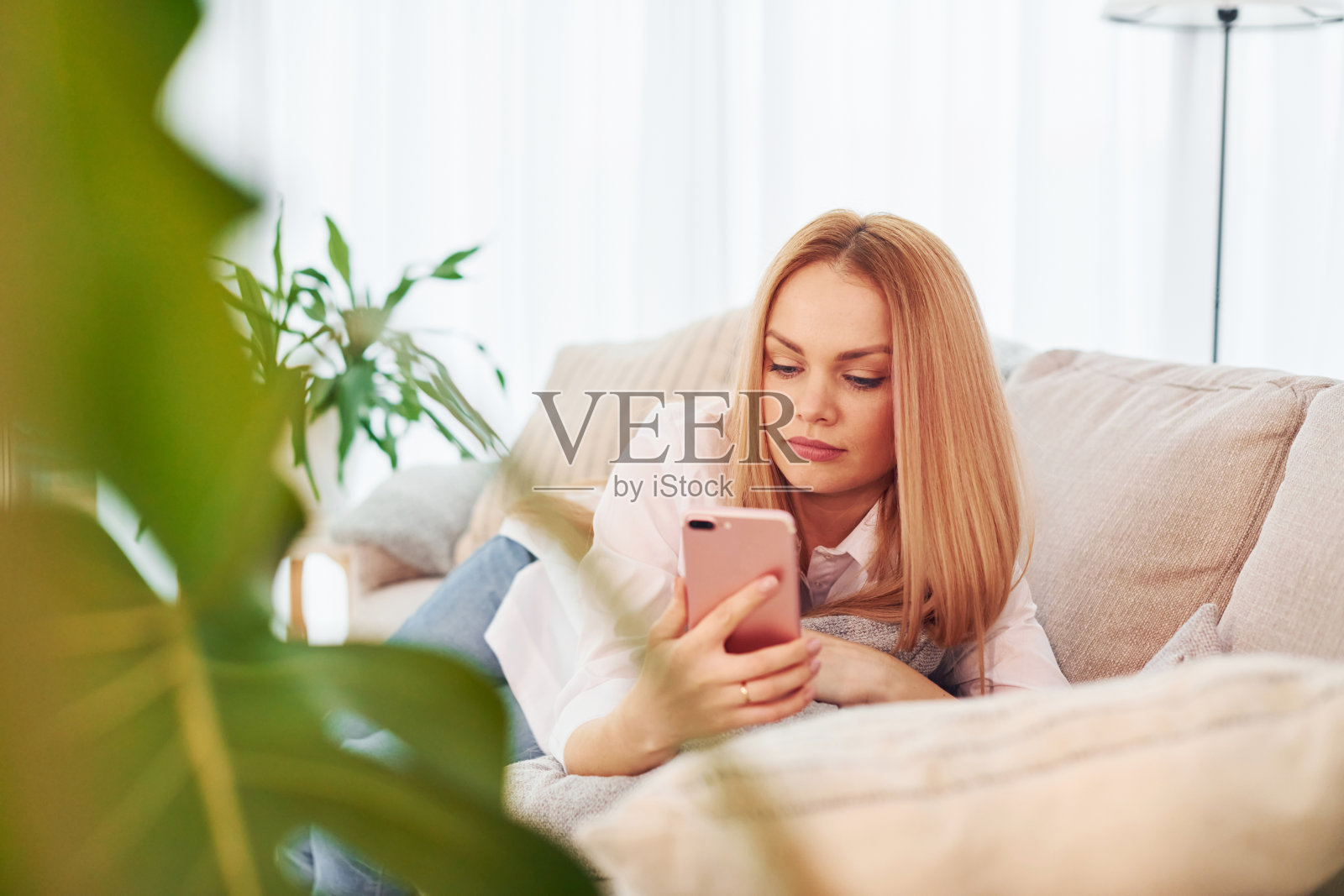 手里拿着手机。穿着白衬衫和牛仔裤的年轻女子在家照片摄影图片