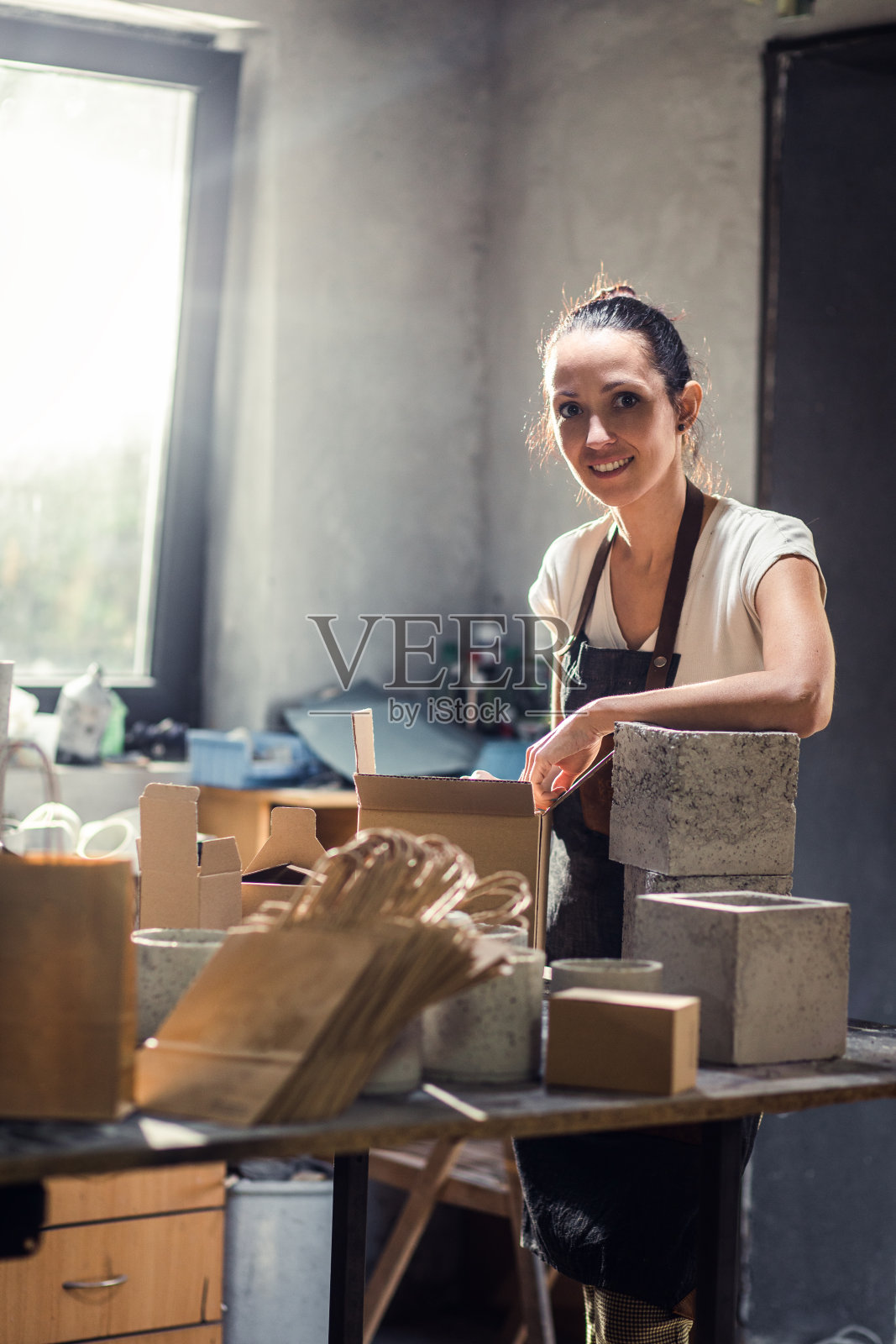 穿着围裙的手工艺人在她的工作室制作装饰混凝土花瓶。照片摄影图片