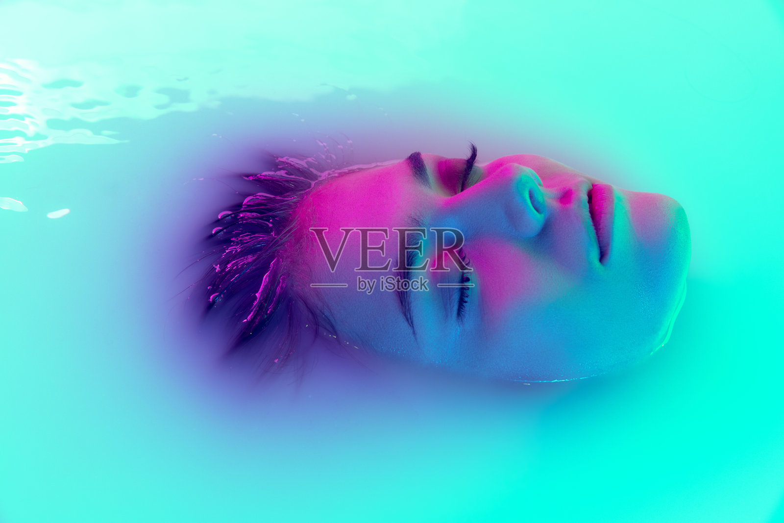 俯视图女性的脸，年轻美丽的女孩在牛奶浴与柔和的发光在蓝绿色霓虹灯。美容、时尚、风格、护肤理念照片摄影图片