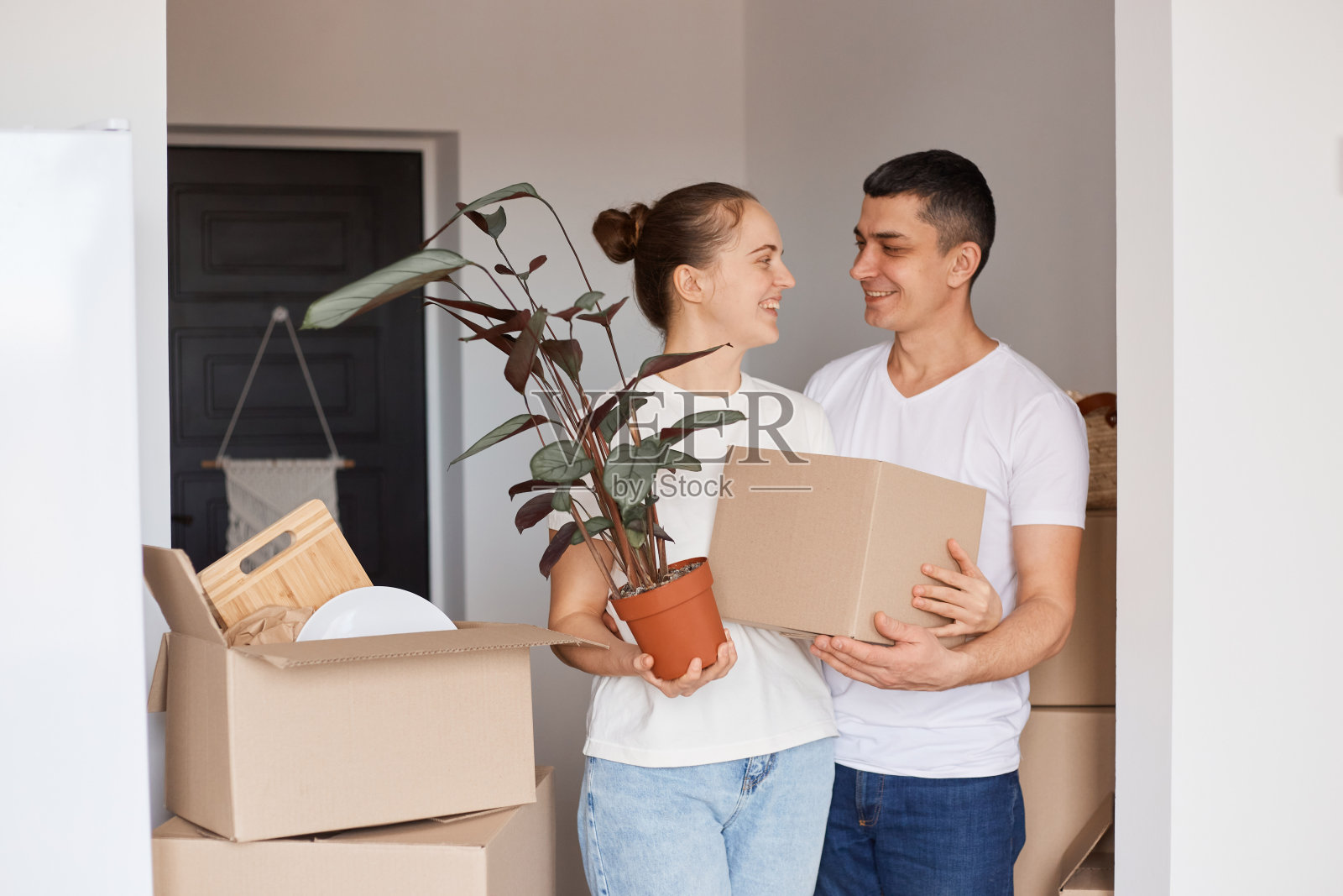 幸福的一家人站在盒子和花盆里的植物，温柔和爱的看着对方，高兴的买了新房子，搬迁，房产，房地产。照片摄影图片