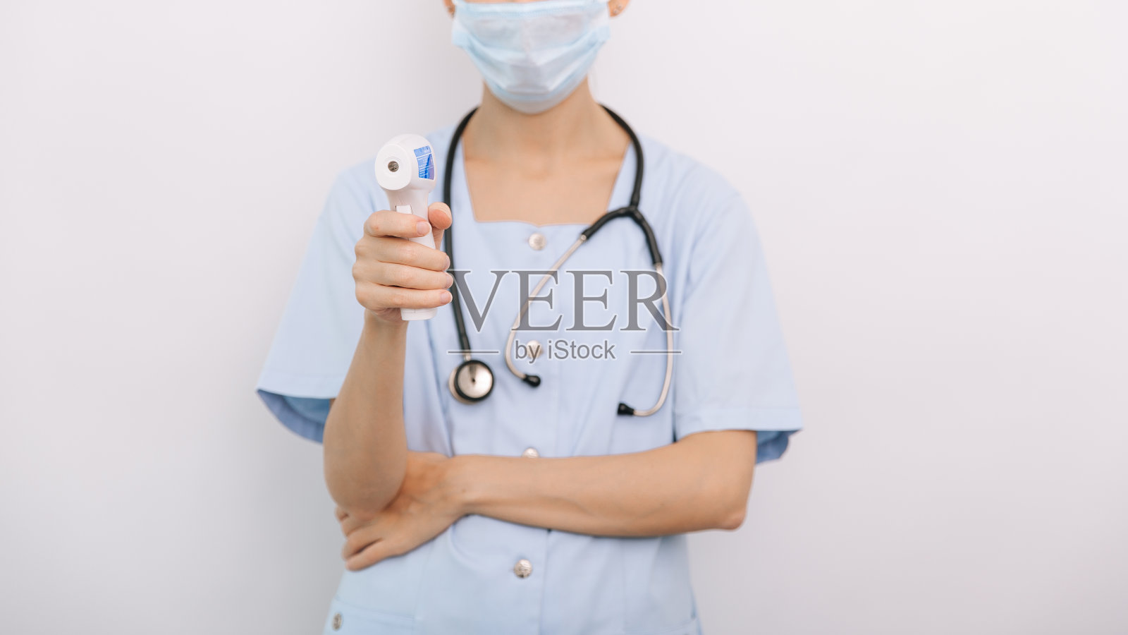 医生手中的测温枪。近距离拍摄的医生戴着防护外科口罩，准备使用红外等距温度计枪检查体温的病毒症状照片摄影图片