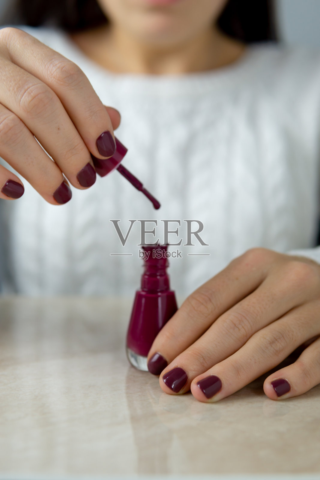 一个认不出来的小女孩手里拿着一款开着的指甲油，还涂了新指甲油。照片摄影图片