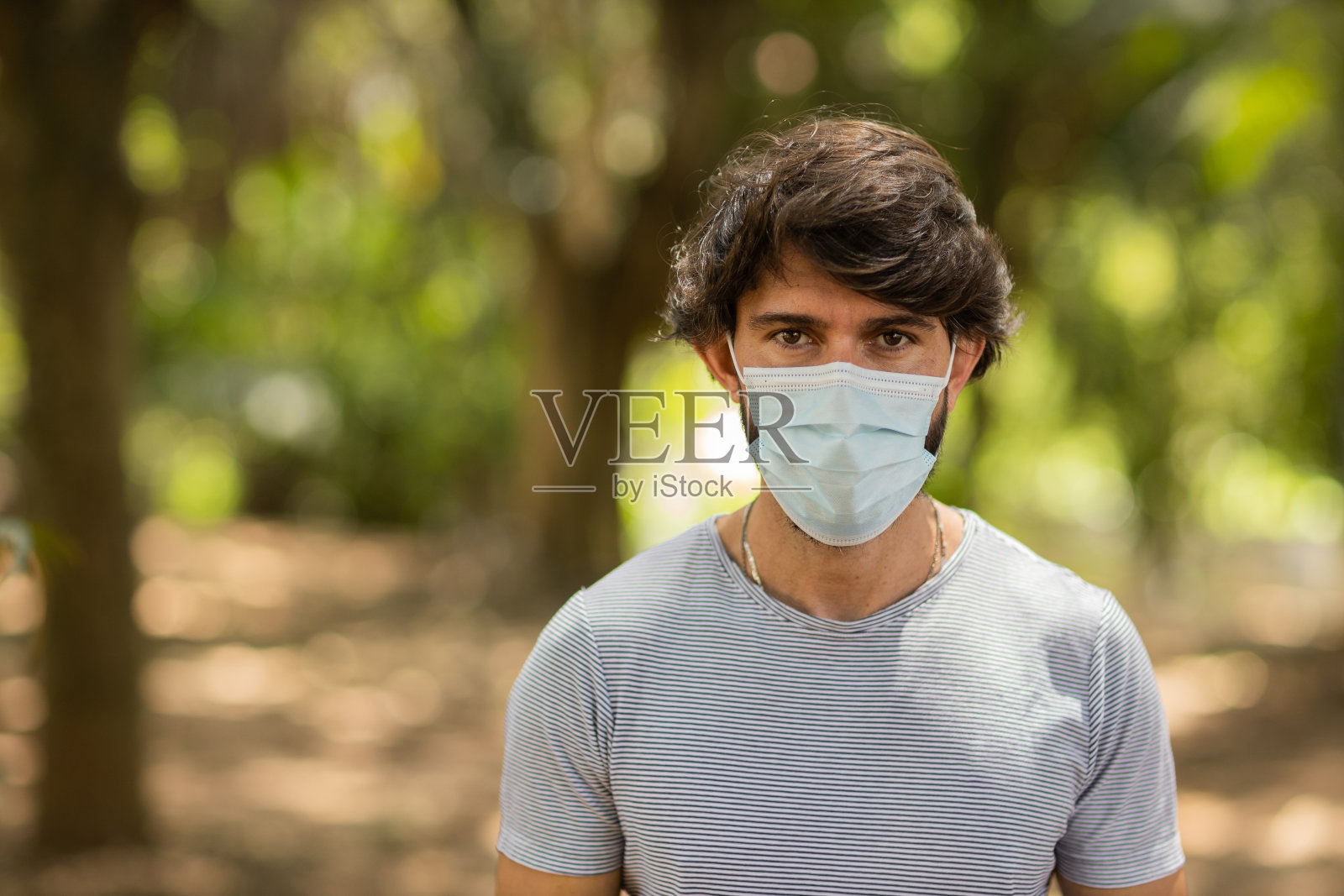 在一个阳光明媚的日子里，在公园里，一名英俊的男子戴着医用防护口罩。高质量的照片。“n照片摄影图片