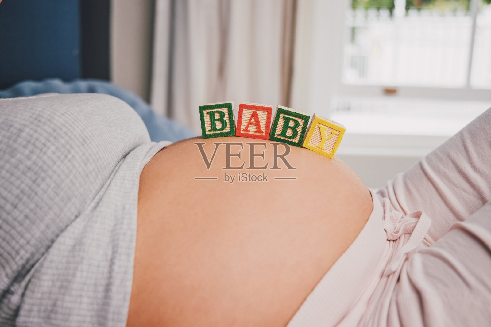 拍摄的是一名孕妇躺在床上，用木块垫着她怀孕的肚子照片摄影图片