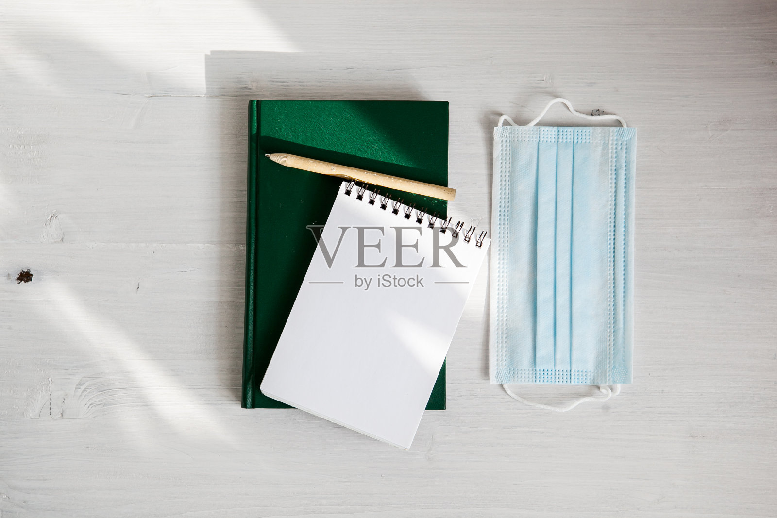 打开白色笔记本上的一个绿色日记本，一个医用口罩和一个绿色树枝照片摄影图片