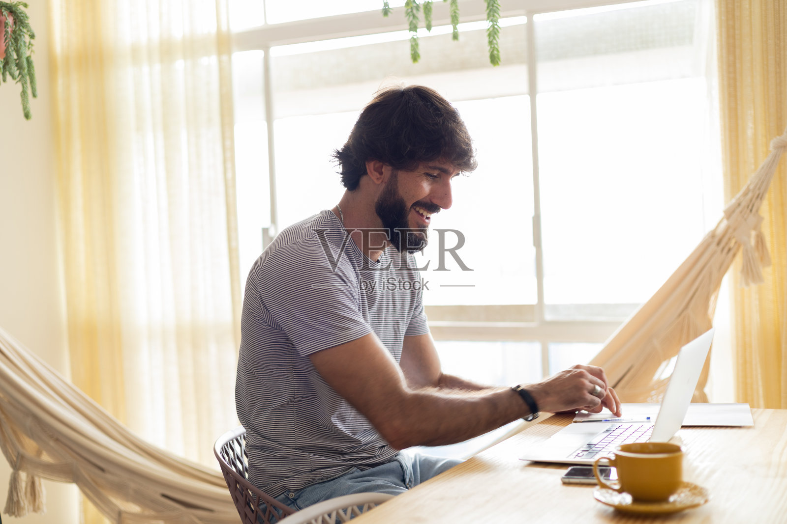 年轻的商人在家里的厨房里工作，笔记本电脑和厨房木桌上的文件。家庭办公室的概念。照片摄影图片