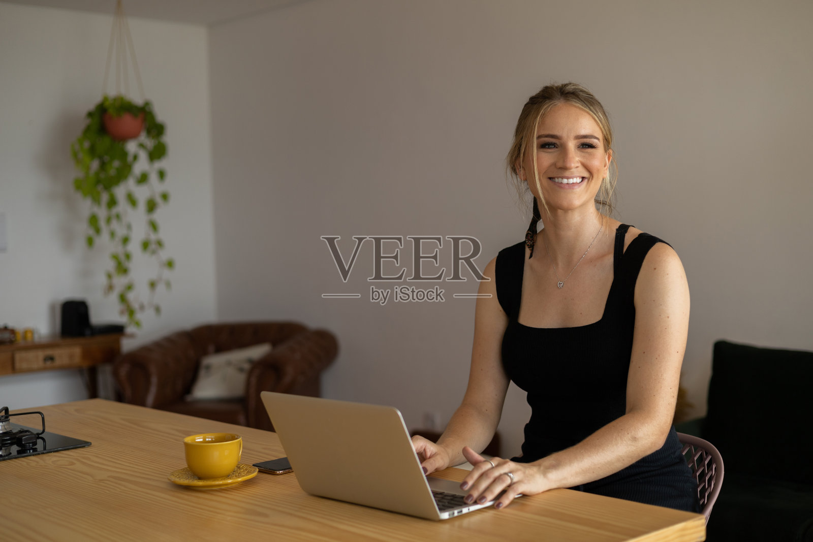 年轻的商人在家里的厨房里工作，笔记本电脑和厨房木桌上的文件。家庭办公室的概念。照片摄影图片