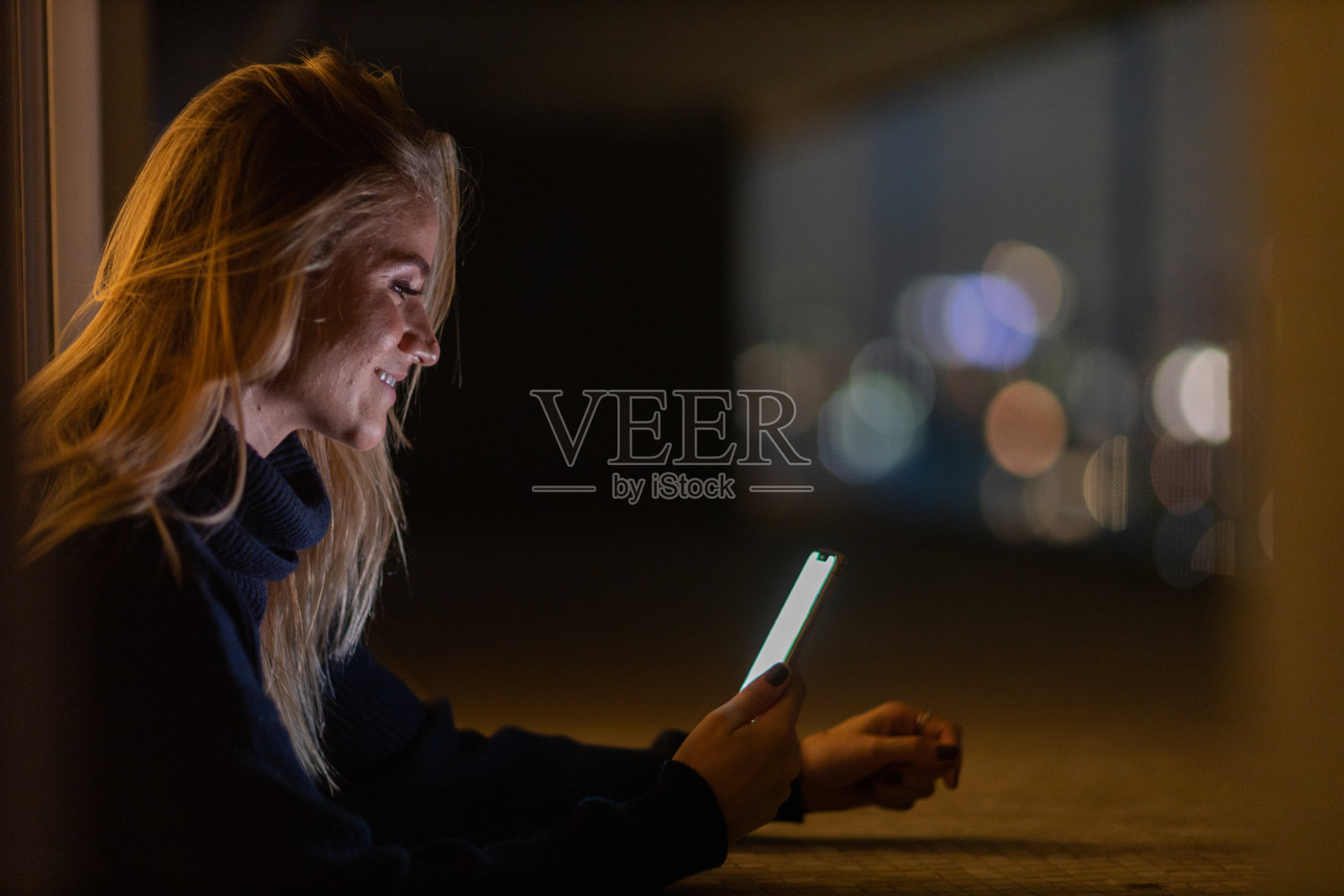 年轻人在夜晚使用智能手机的前视图，城市景观在背景中。高质量的照片照片摄影图片