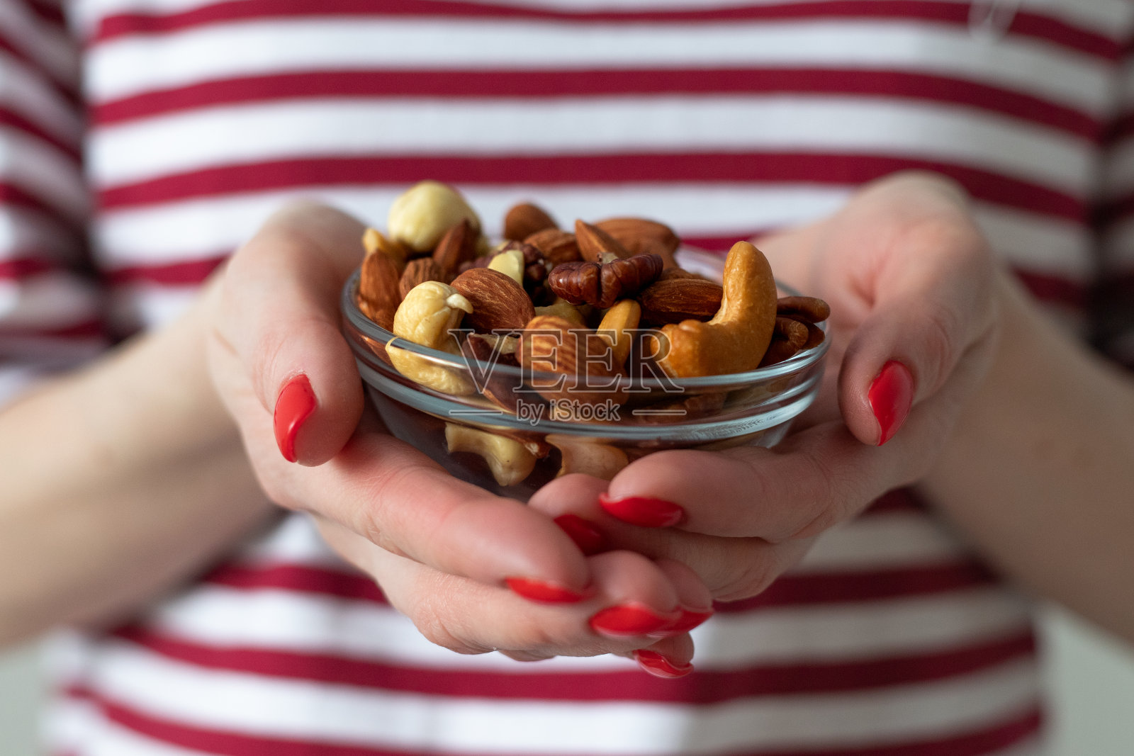 涂着红色指甲的女性手握着透明的玻璃板，背景是一件红白相间的条纹t恤照片摄影图片