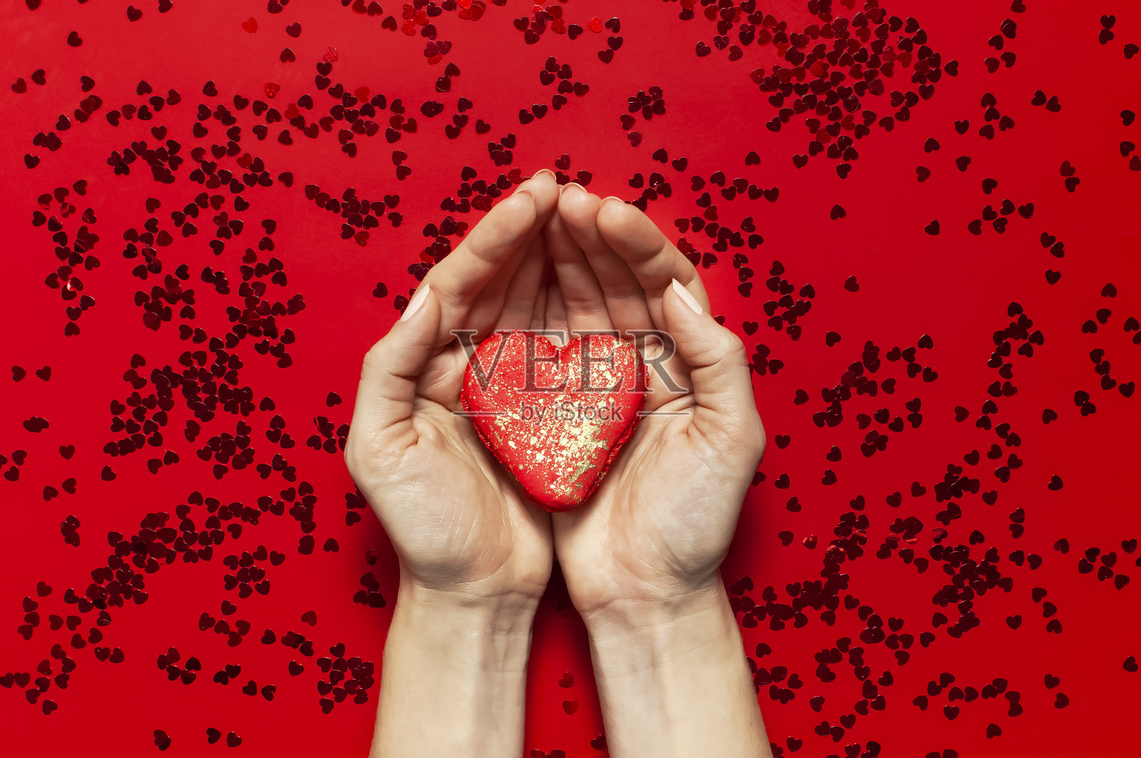 女人的手握红色心形马卡龙蛋糕和红色背景上的五彩纸花topview平坦。创意构成情人节爱的概念生日礼物母亲节节日背景照片摄影图片