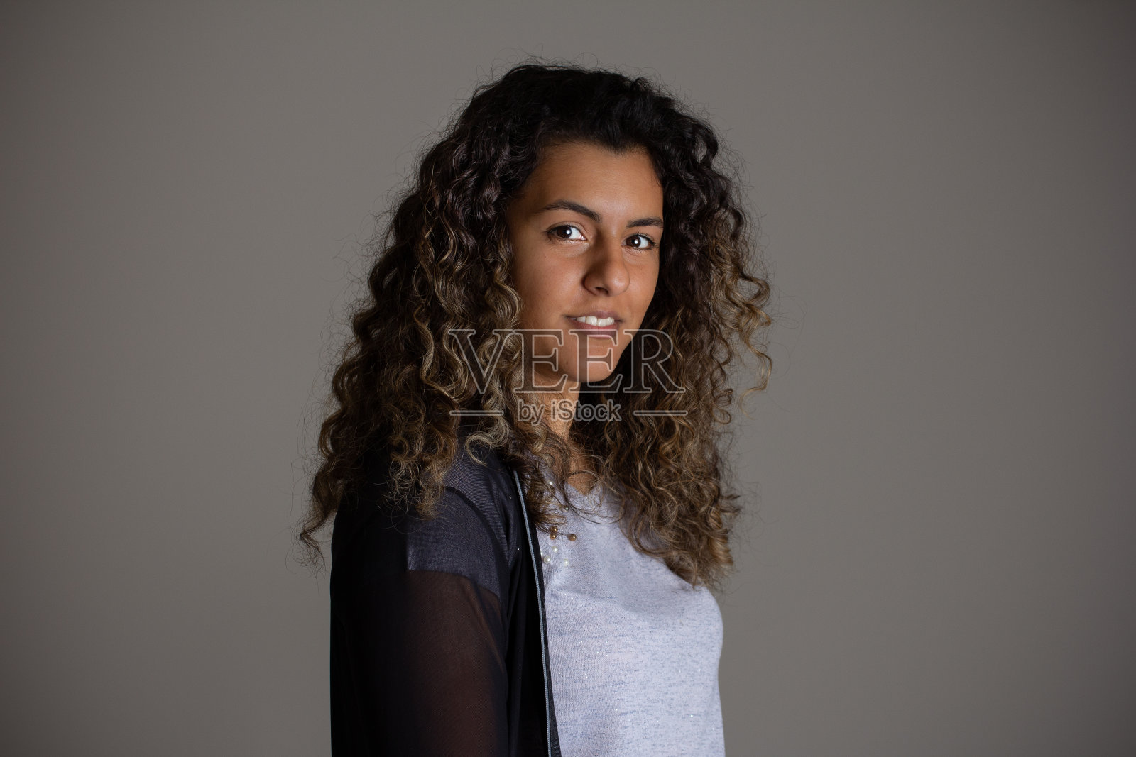 黑色卷发女孩摆姿势拍照。可爱的女人和大波浪头发的侧面视图。照片摄影图片