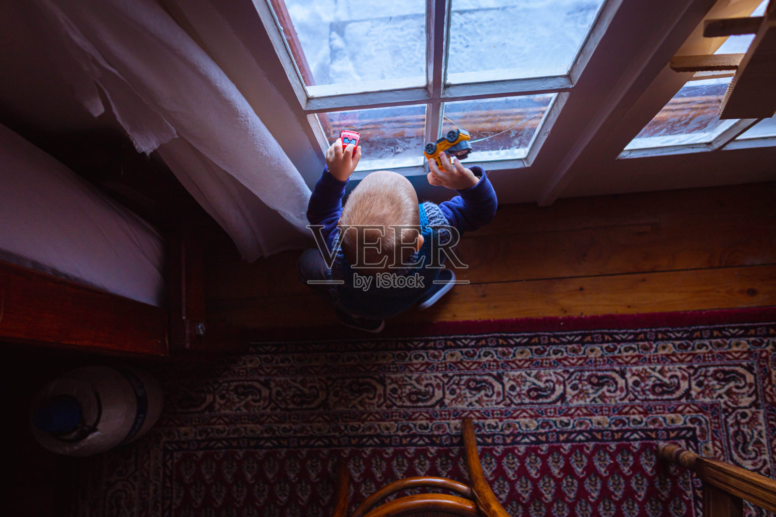 可爱的蹒跚学步的小男孩在车窗上玩汽车玩具照片摄影图片