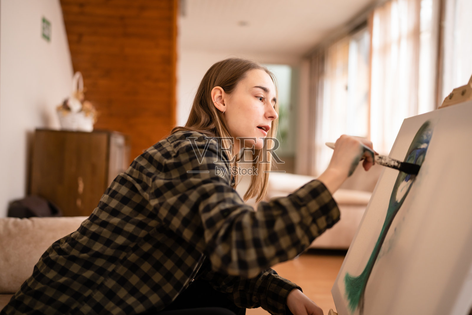 一位年轻美丽的白人女性艺术家坐在床上沙发在画布上绘画，拿着画笔艺术和创意专业或爱好概念真实的人侧视复制空间照片摄影图片