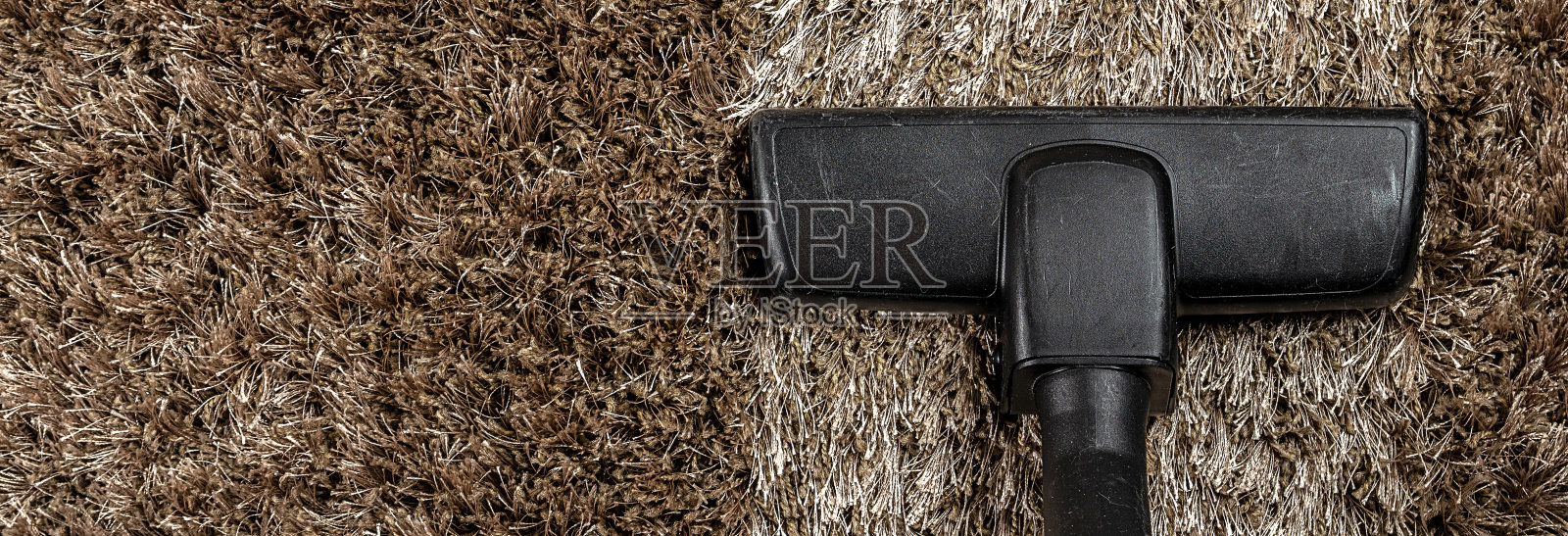 吸尘器的头放在毛茸茸的地毯上，上面有一条特别干净的带子。做家务。全景横幅。照片摄影图片