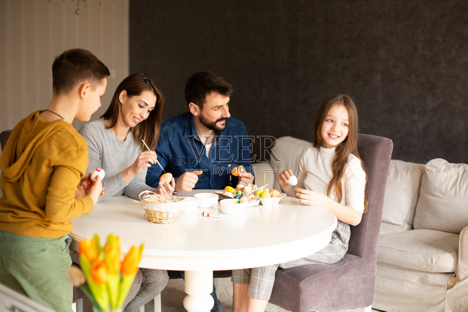 家长们和孩子们一起在餐厅的餐桌上为复活节彩蛋上色。照片摄影图片