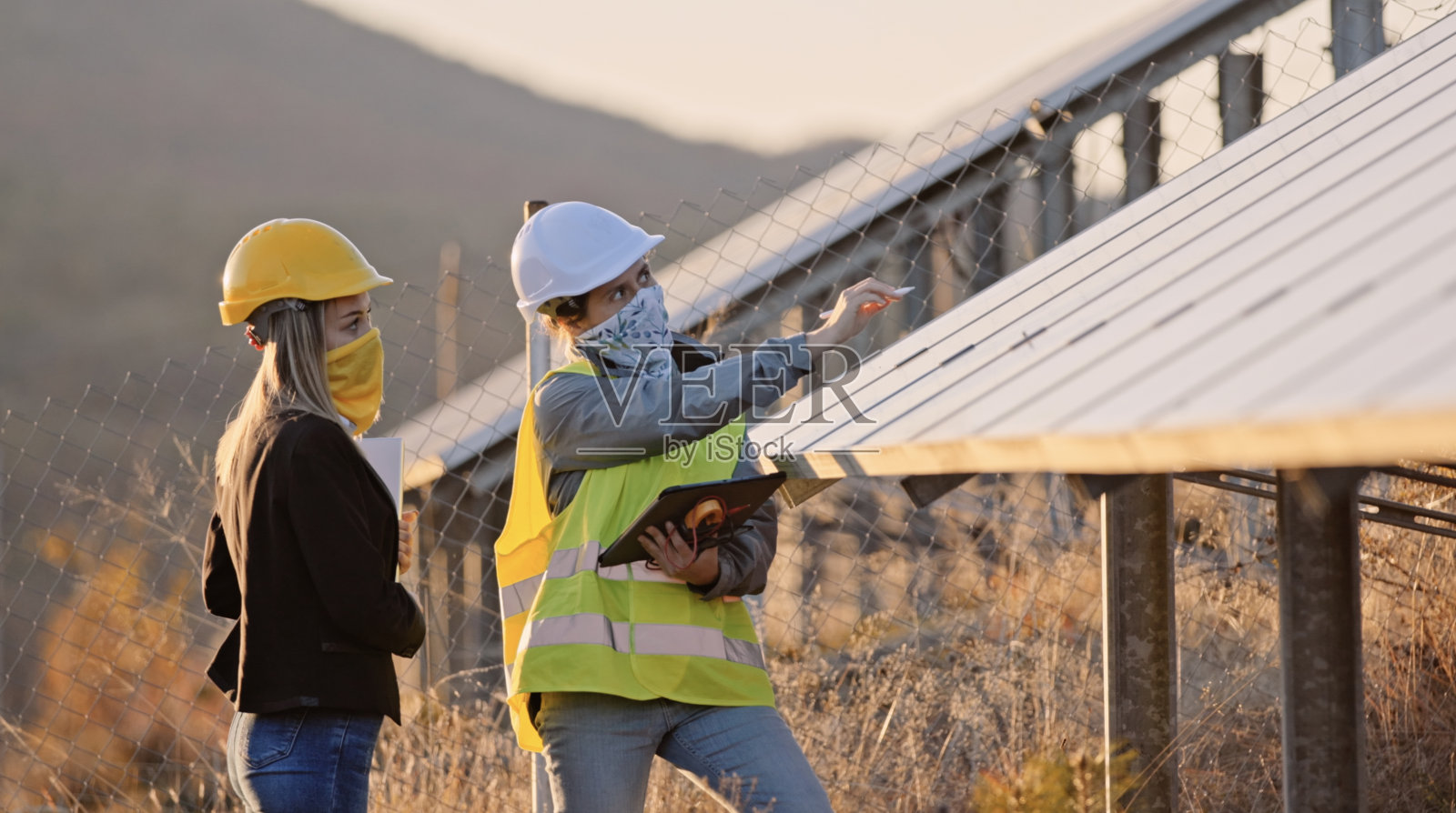在太阳能发电厂工作的女性工程师。团队合作在COVID-19。可再生能源系统。太阳能城市。照片摄影图片