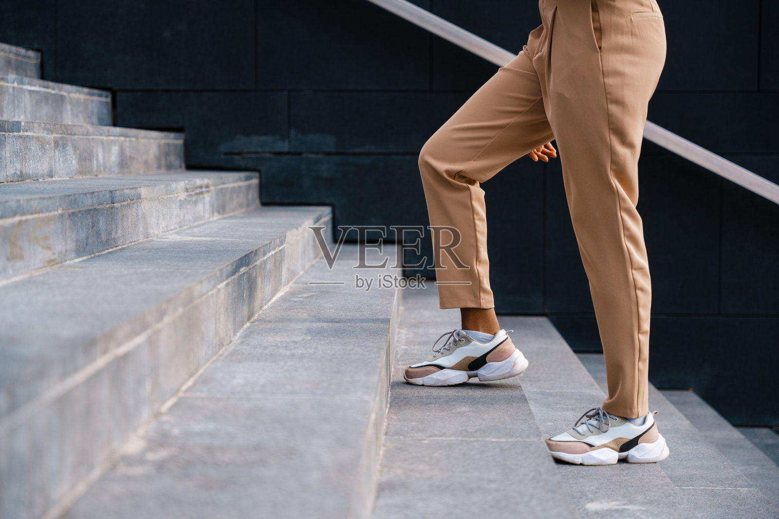 一个穿着米色夏装长裤和运动鞋的女人站在楼梯上照片摄影图片