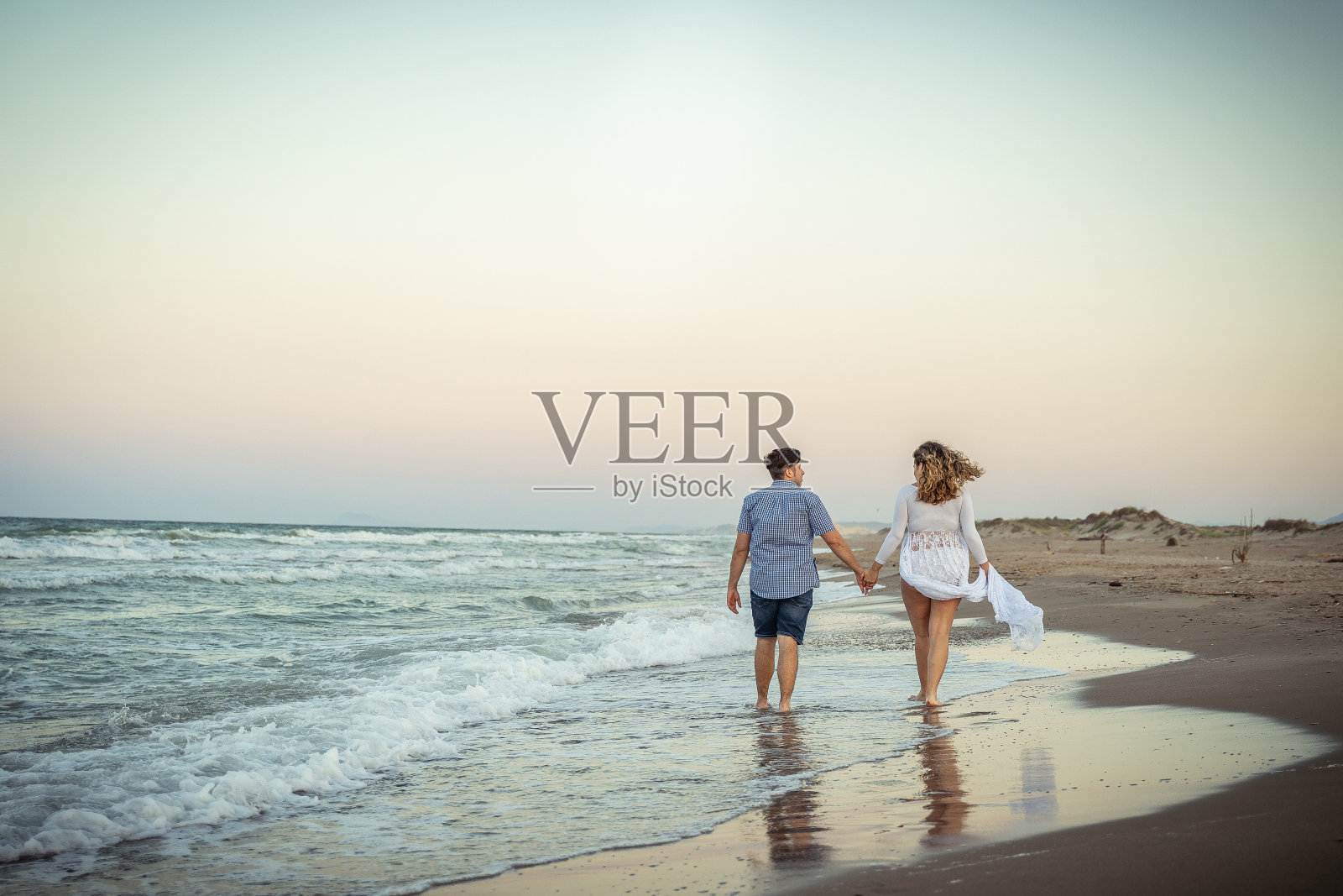 男男女女在夏日夕阳下光着脚走在沙滩上照片摄影图片