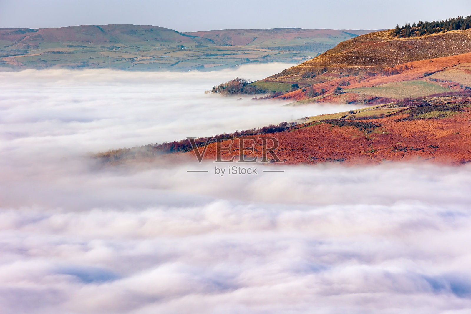 在威尔士的布雷肯信标上，山脉和树木通过低空的雾和云倒转显示出来照片摄影图片