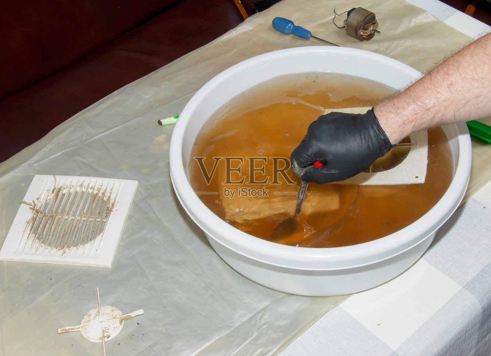 在氢氧化钠水溶液中清洗非常脏的厨房排气扇的塑料部件。一个人戴着防护手套工作。照片摄影图片