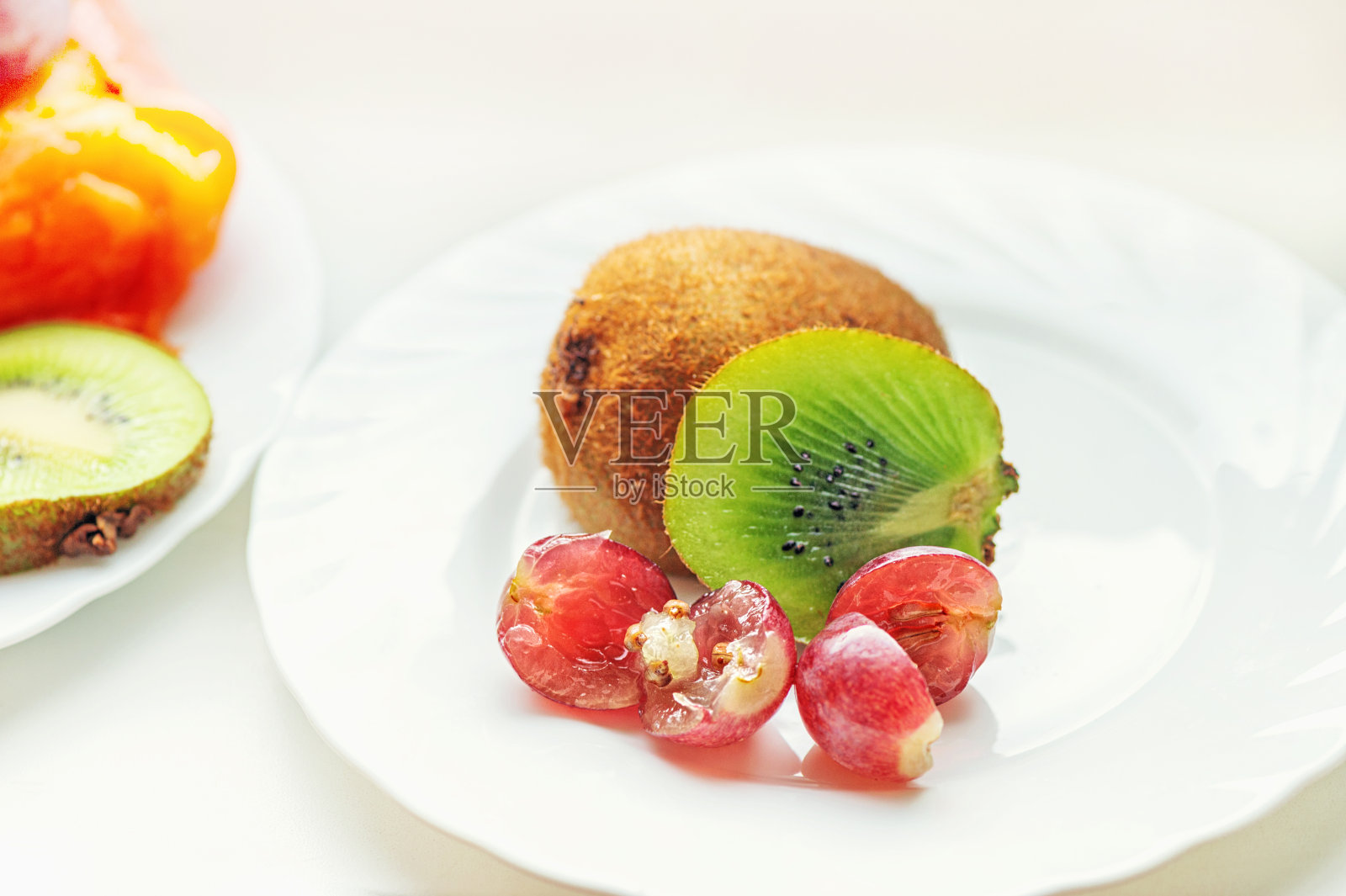 盘子上是半只成熟多汁的绿色猕猴桃和白色盘子上的葡萄。关闭了。光单色背景照片摄影图片