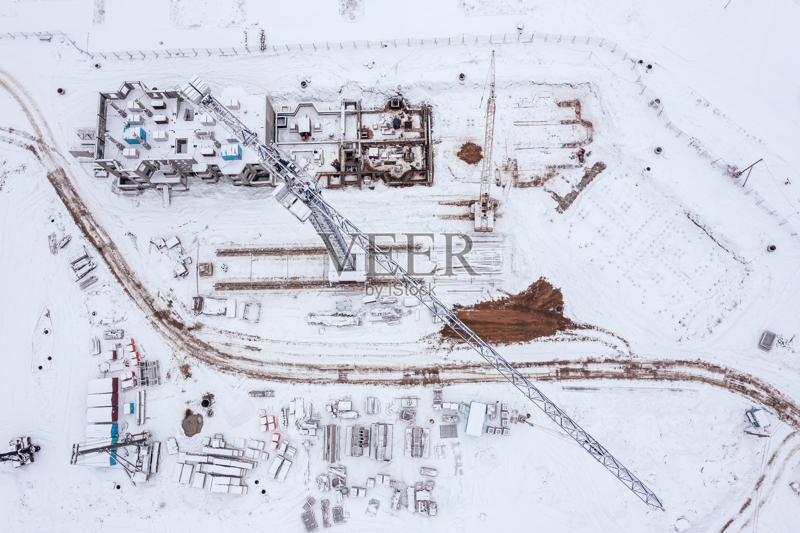 鸟瞰下雪的建筑工地与新公寓大楼，机械和建筑材料照片摄影图片