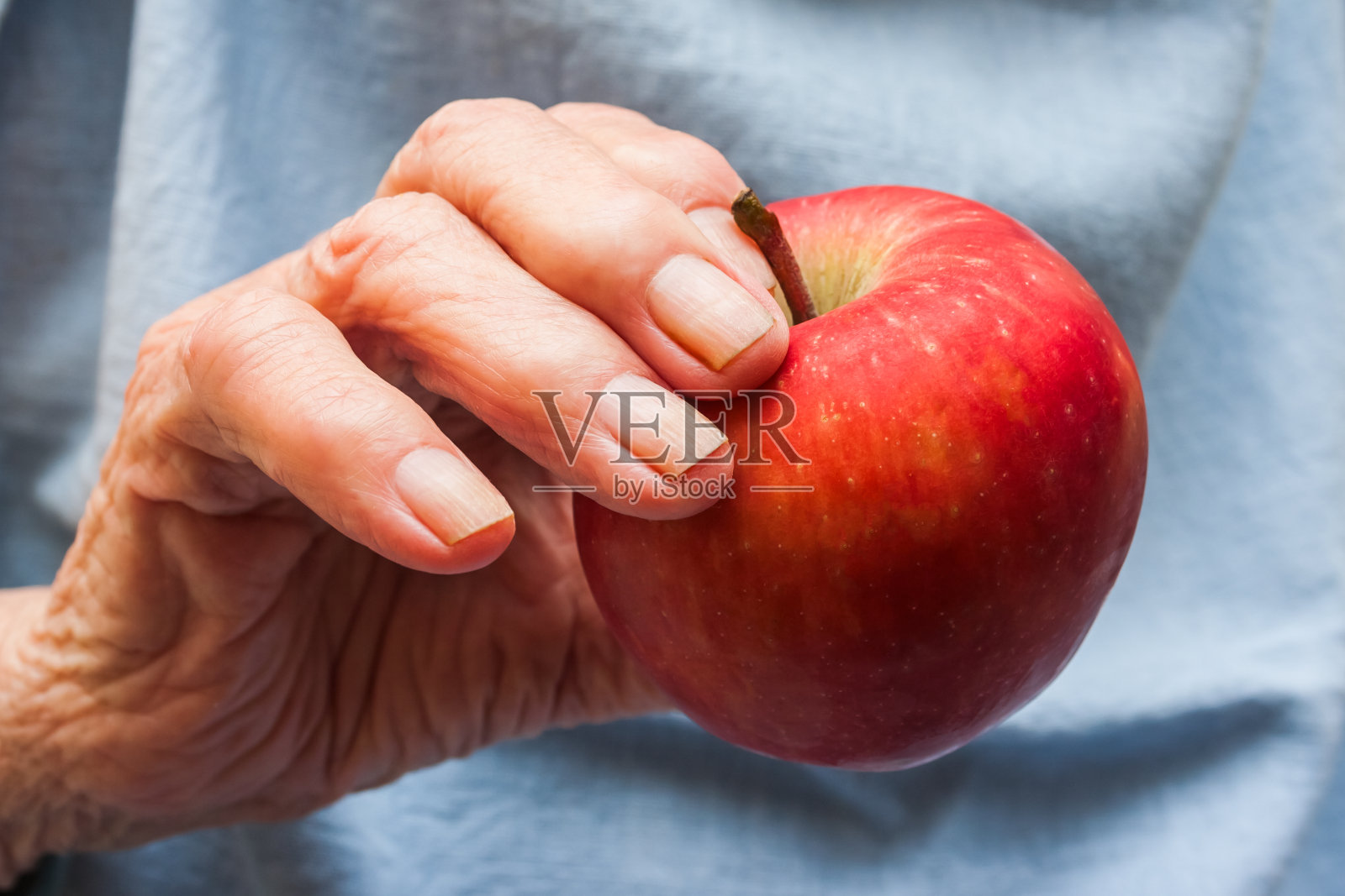一个拿着红苹果的老妇人的手。长寿的概念。老年人的一天。照片摄影图片