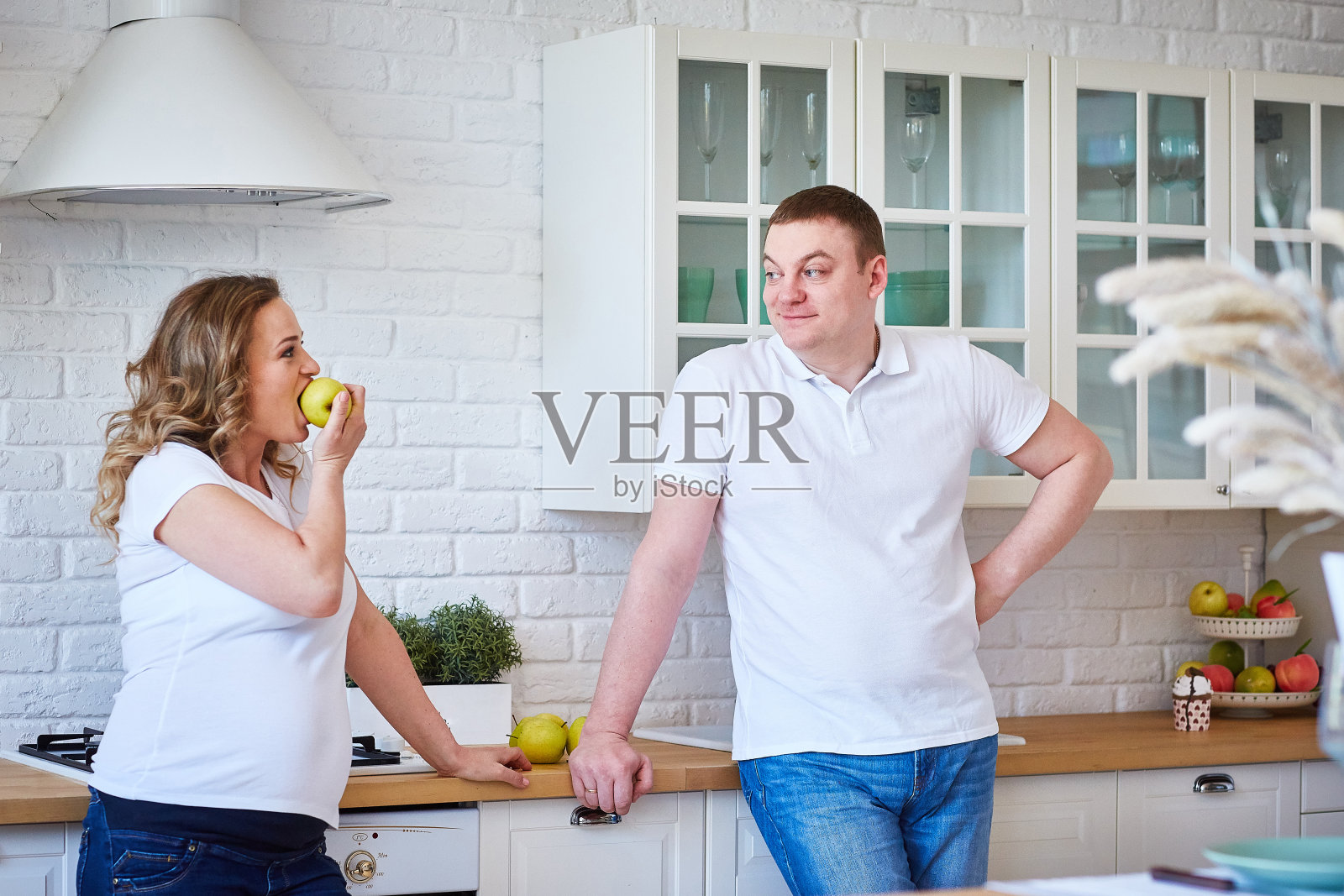 孕妇和丈夫在家里的厨房里吃水果。这个家庭正在等待一个孩子的出生。照片摄影图片