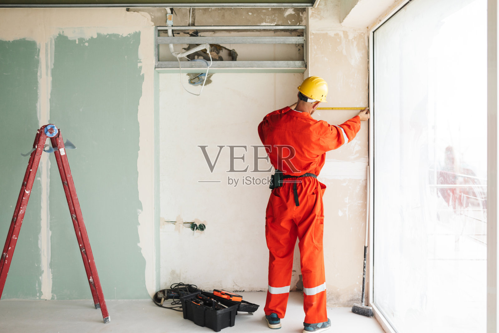 穿着橙色工作服、戴着安全帽、使用卷尺的建筑工照片摄影图片