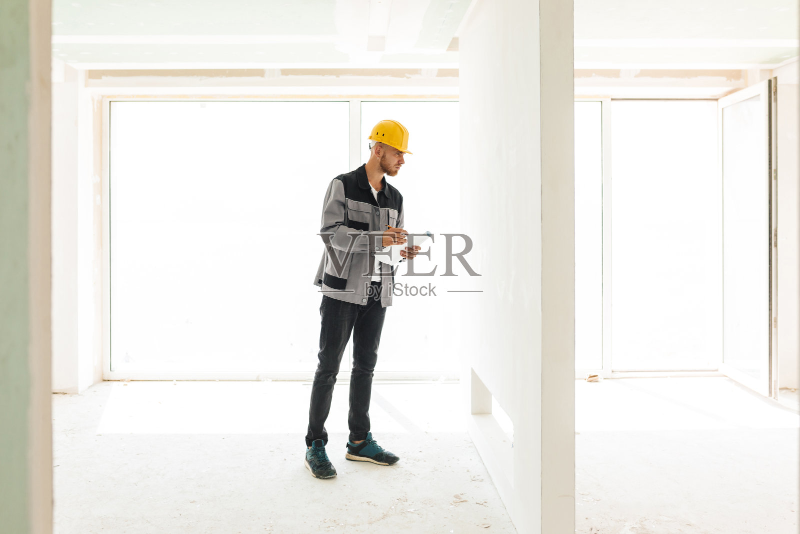 年轻的工程师穿着工作服，戴着黄色安全帽，手持平面图o照片摄影图片