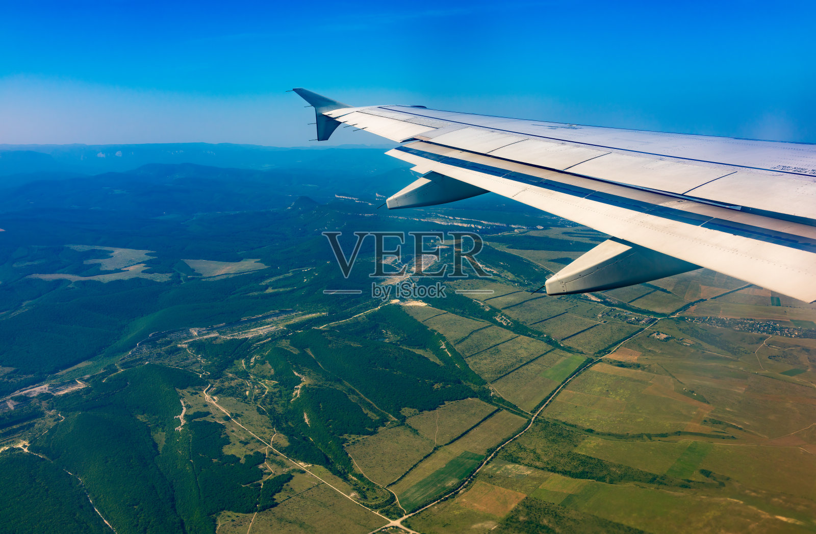 飞机的机翼，蓝天和绿色的土地着陆。飞机窗口视图。照片摄影图片