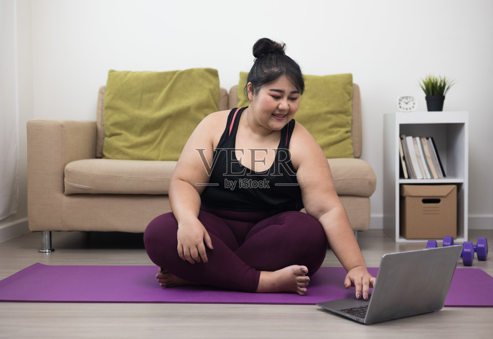 年轻的亚洲运动妇女加号坐练习瑜伽课。在家里进行腿部伸展训练，以保持健康和身材。通过笔记本电脑视频在线课程学习技能。照片摄影图片