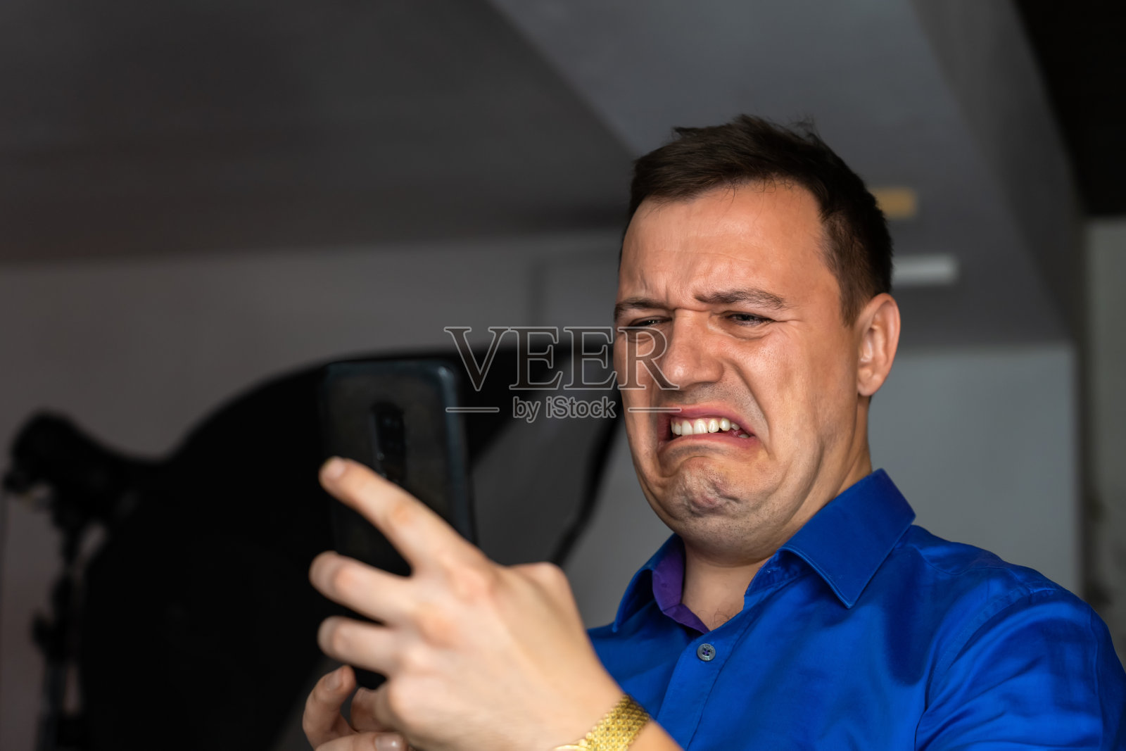 恼怒的千禧一代男子厌恶地盯着室内的智能手机屏幕。经理的肖像，畏畏缩缩地看着手机屏幕，神经质的，糟糕的笑话或不适当的内容照片摄影图片