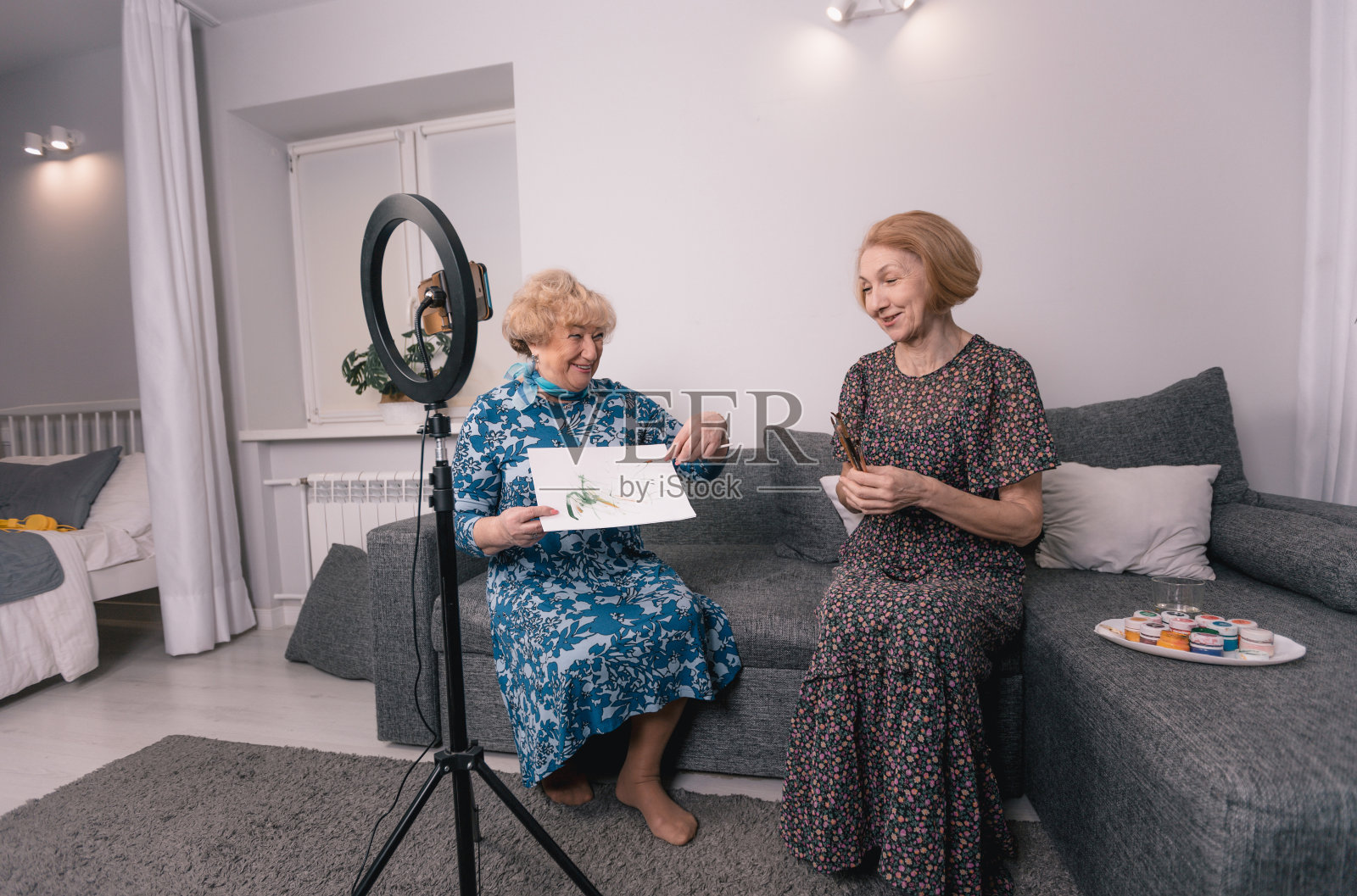 2名老年妇女正坐在沙发上用智能手机拍摄视频博客。绘画，艺术家，画笔，笔触在纸上。日常生活美学。照片摄影图片