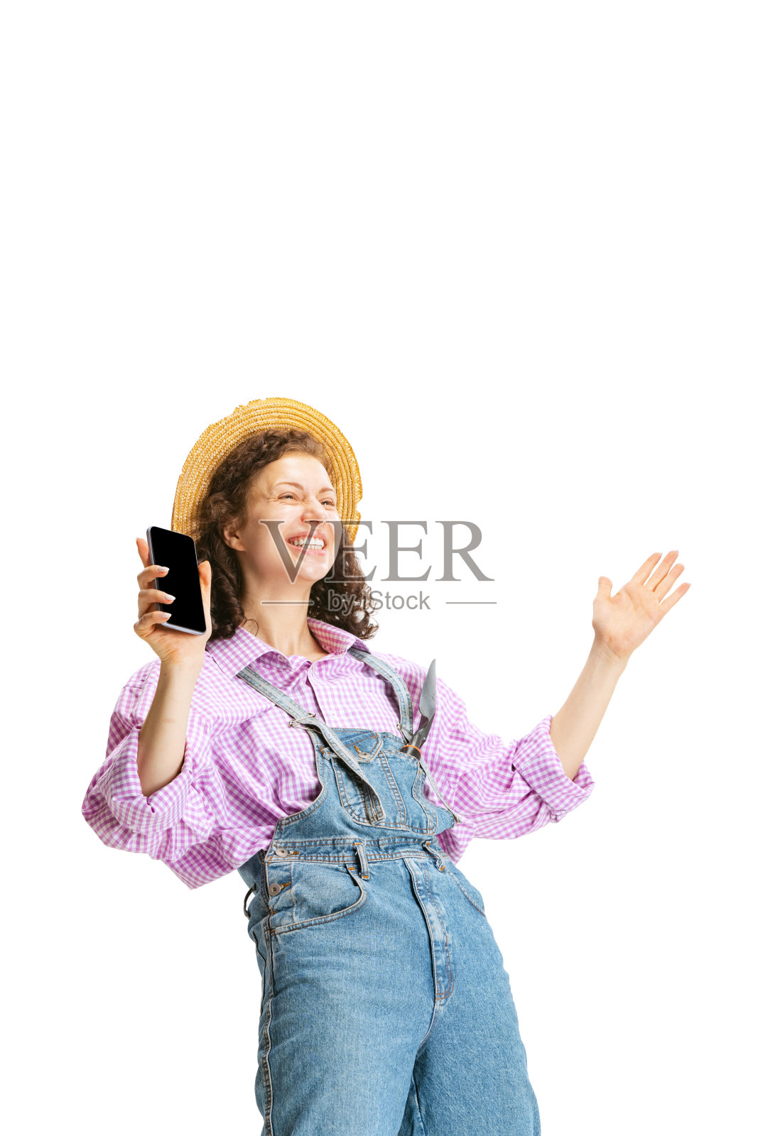 兴奋的年轻女孩，女园丁在工作制服和帽子使用手机孤立在白色背景。工作、情感、农学、生态的概念照片摄影图片
