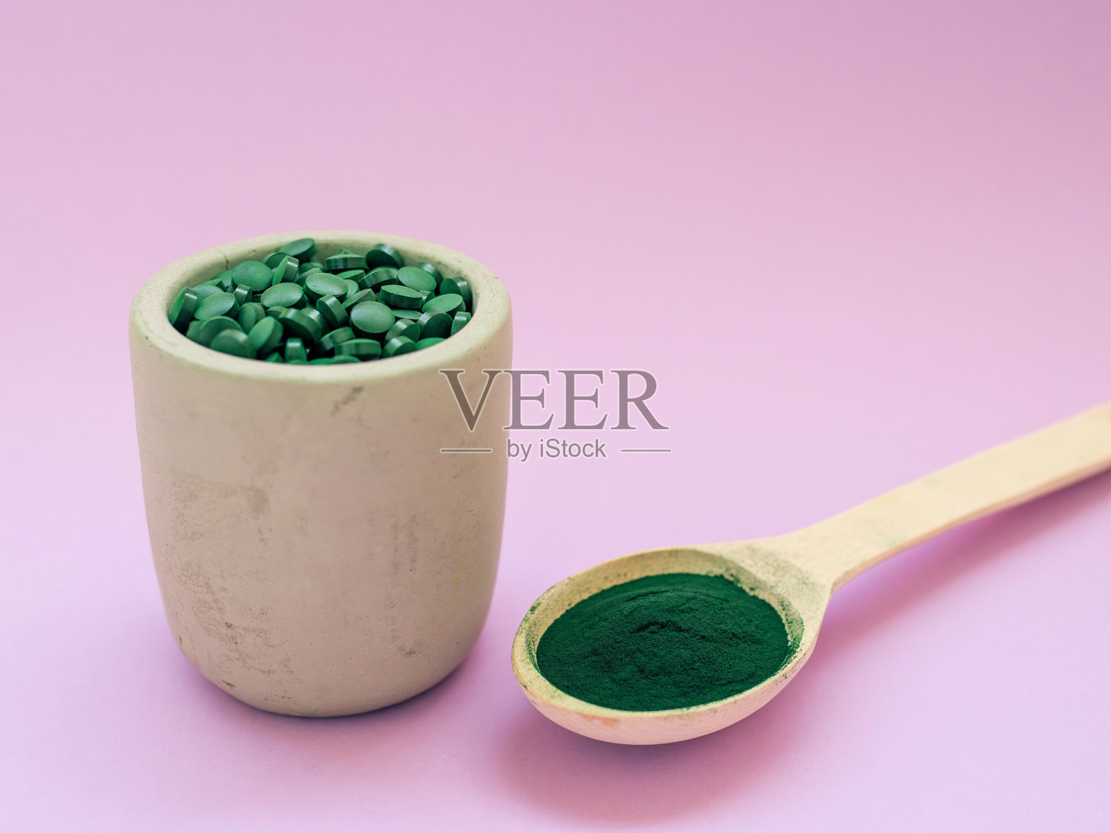 绿色夏威夷螺旋藻在大汤匙药丸粉红色的背景。照片摄影图片