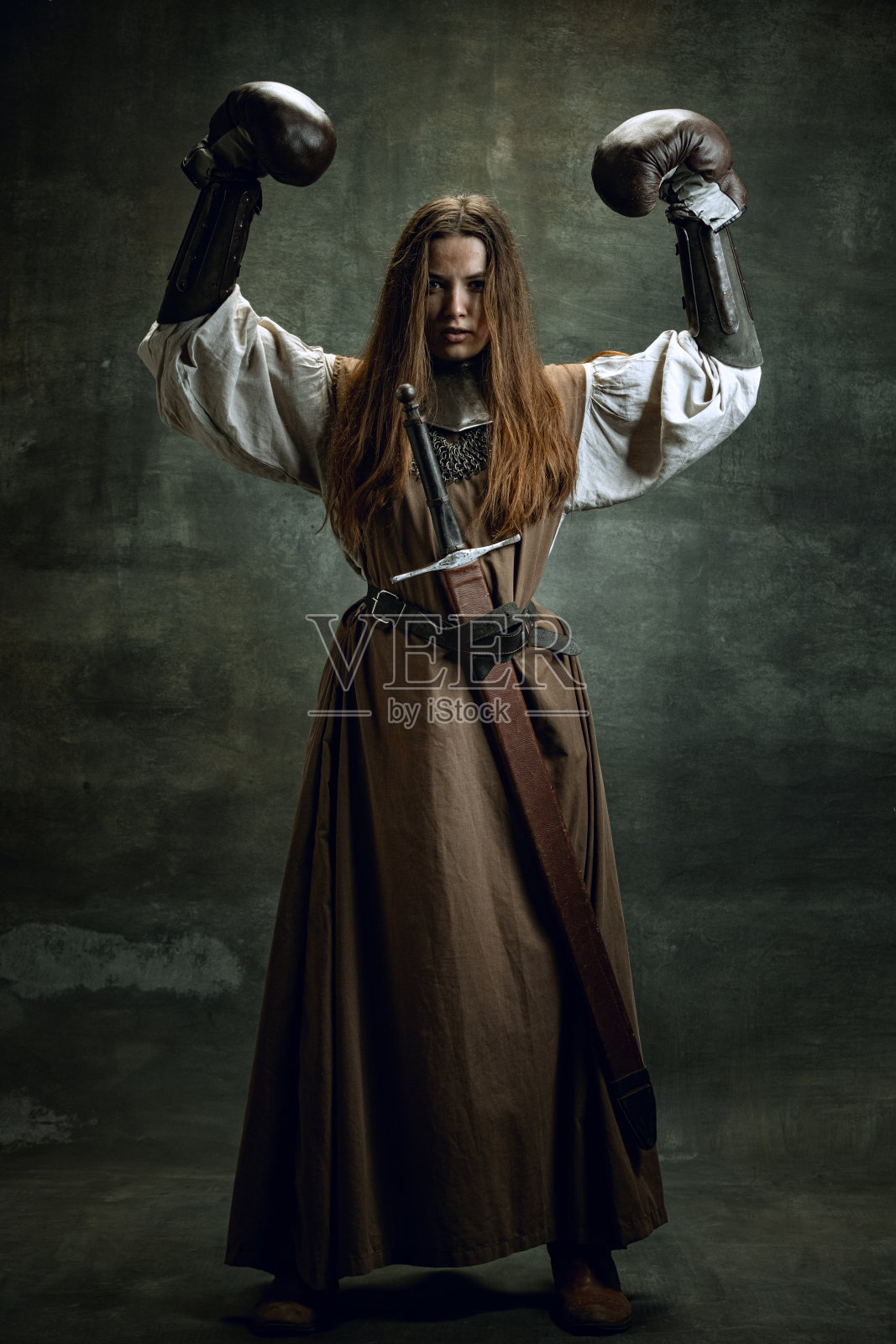 勇敢的女孩，中世纪武士或骑士的肖像与肮脏的受伤的脸在拳击手套孤立在黑暗的复古背景。比较时代和历史照片摄影图片