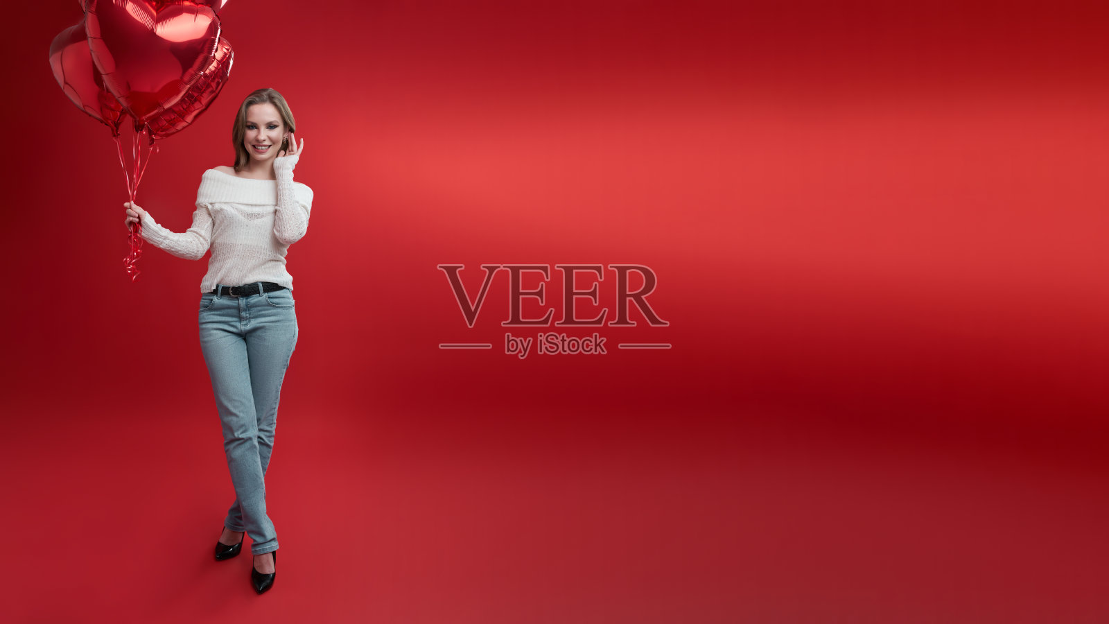 身着休闲服装的年轻女子拿着一束红色背景的气球。照片摄影图片